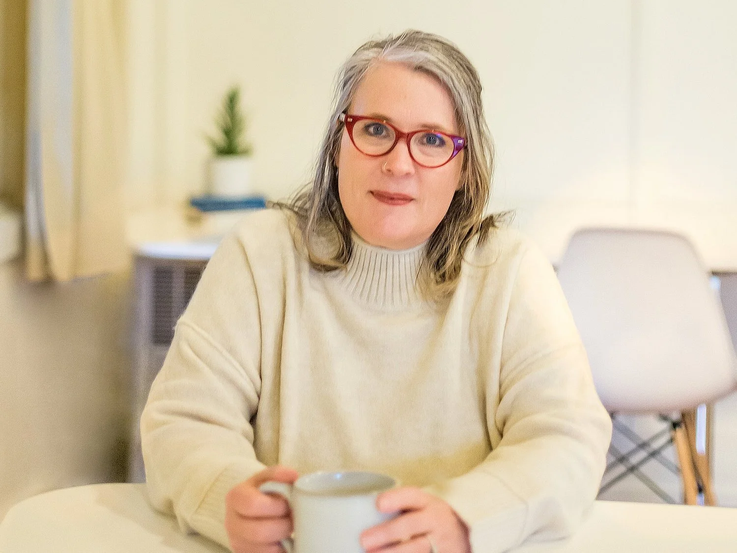Person with glasses holding a mug at a table