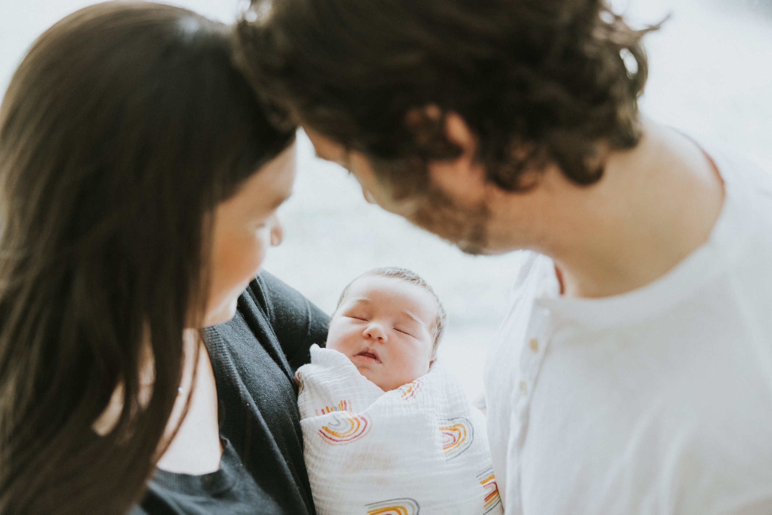 A close-up shot of loving parents gazing down at their peacefully sleeping newborn, enveloped in a warm, intimate moment.