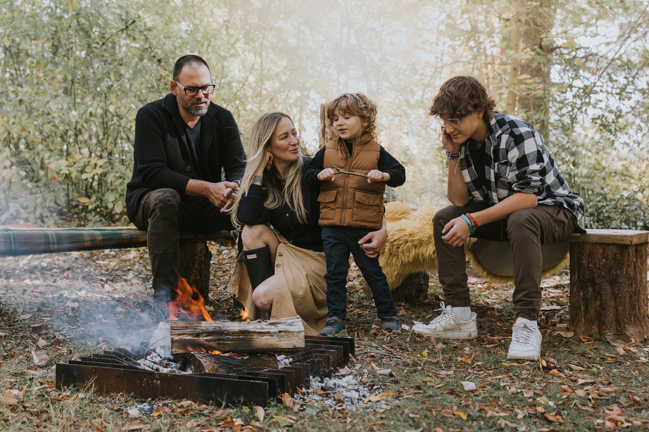 A family gathered around a campfire in an outdoor nature setting, sharing smiles and conversation.