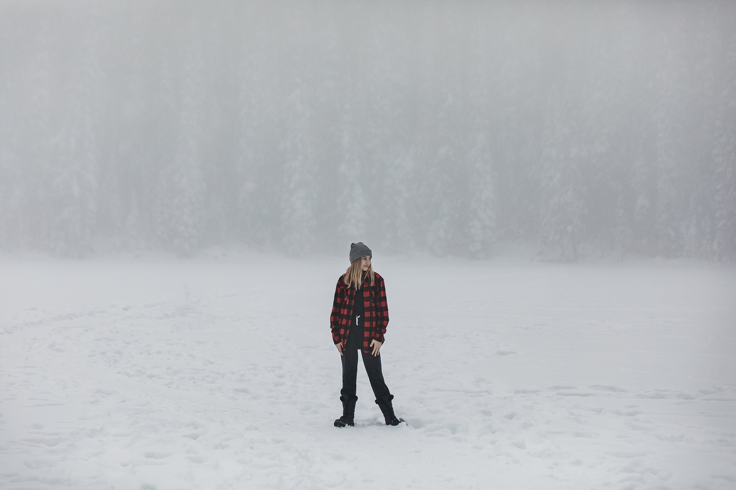 A solo portrait of a person standing in a snowy, foggy forest, creating a mysterious winter atmosphere.