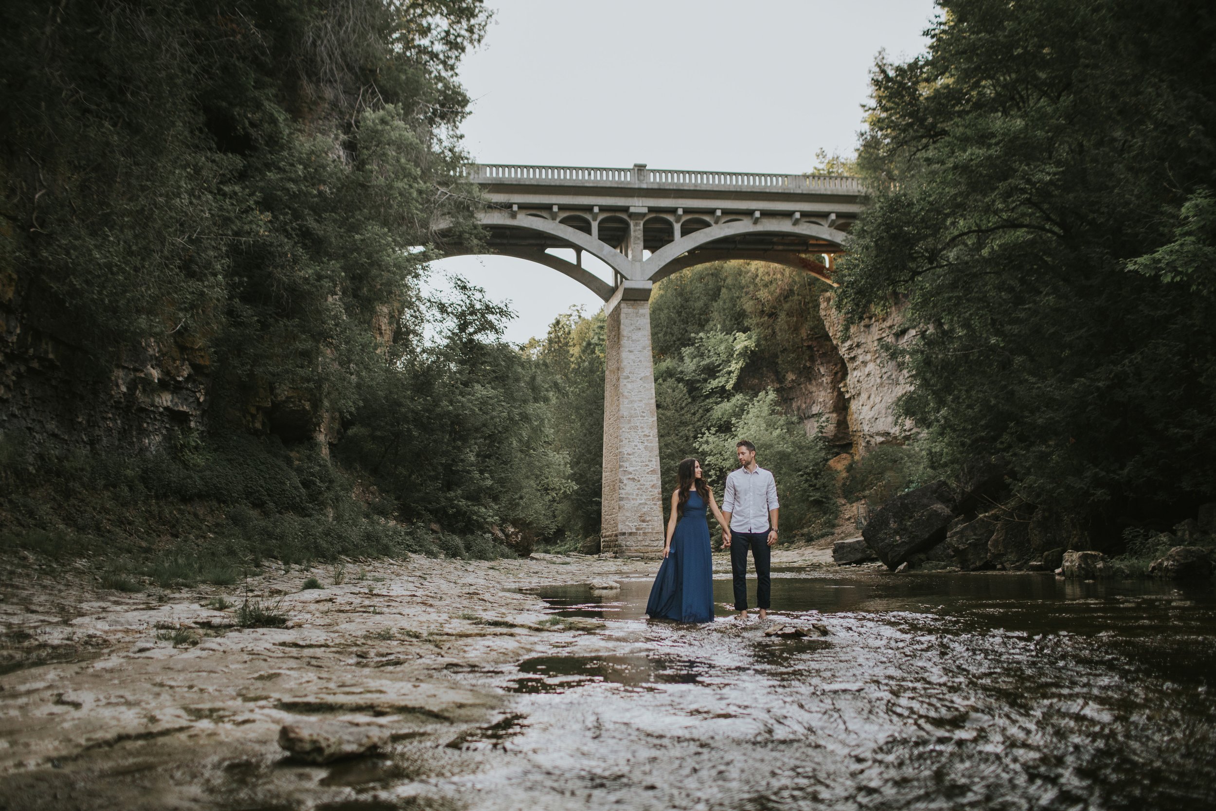 A couple shares a kiss during an engagement session by the river at Elora Gorge at sunset.