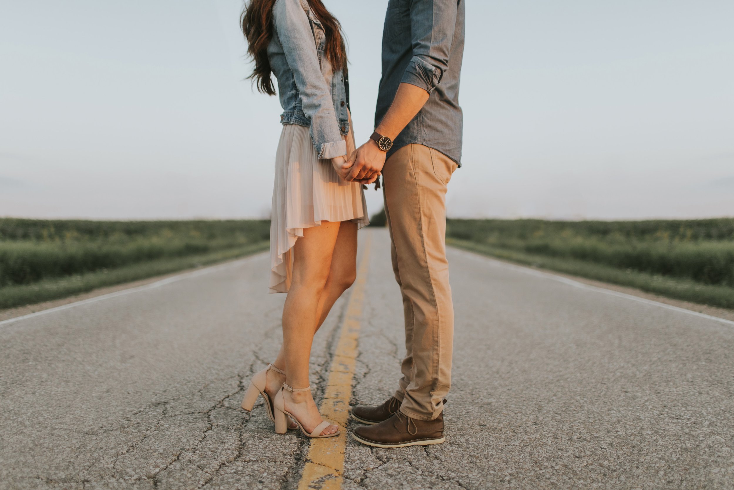 A couple holds hands while standing in the middle of a rural road, symbolizing their journey together during an engagement session.