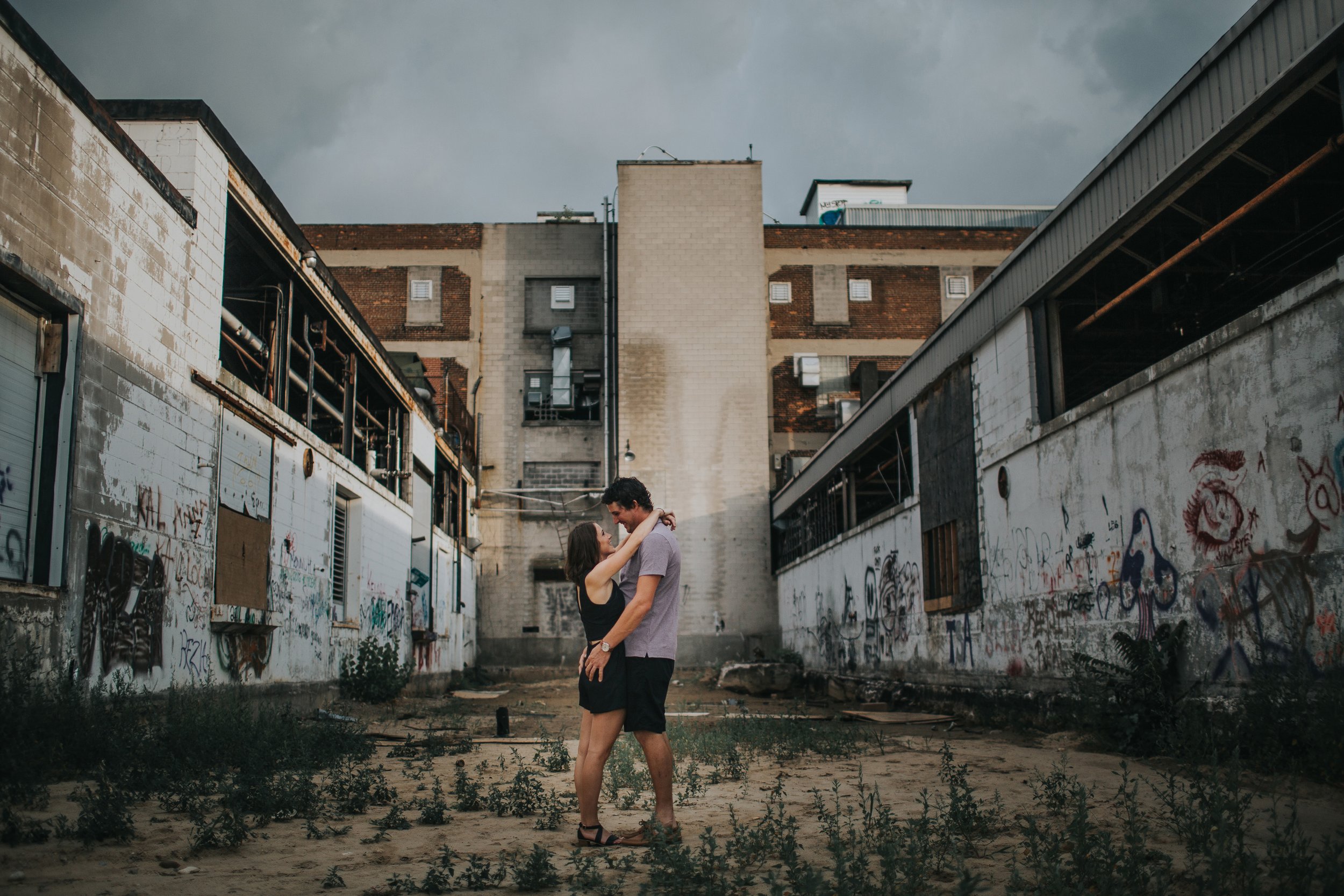 A couple embracing in an abandoned warehouse with graffiti-covered walls, blending urban grit with a tender moment of connection.