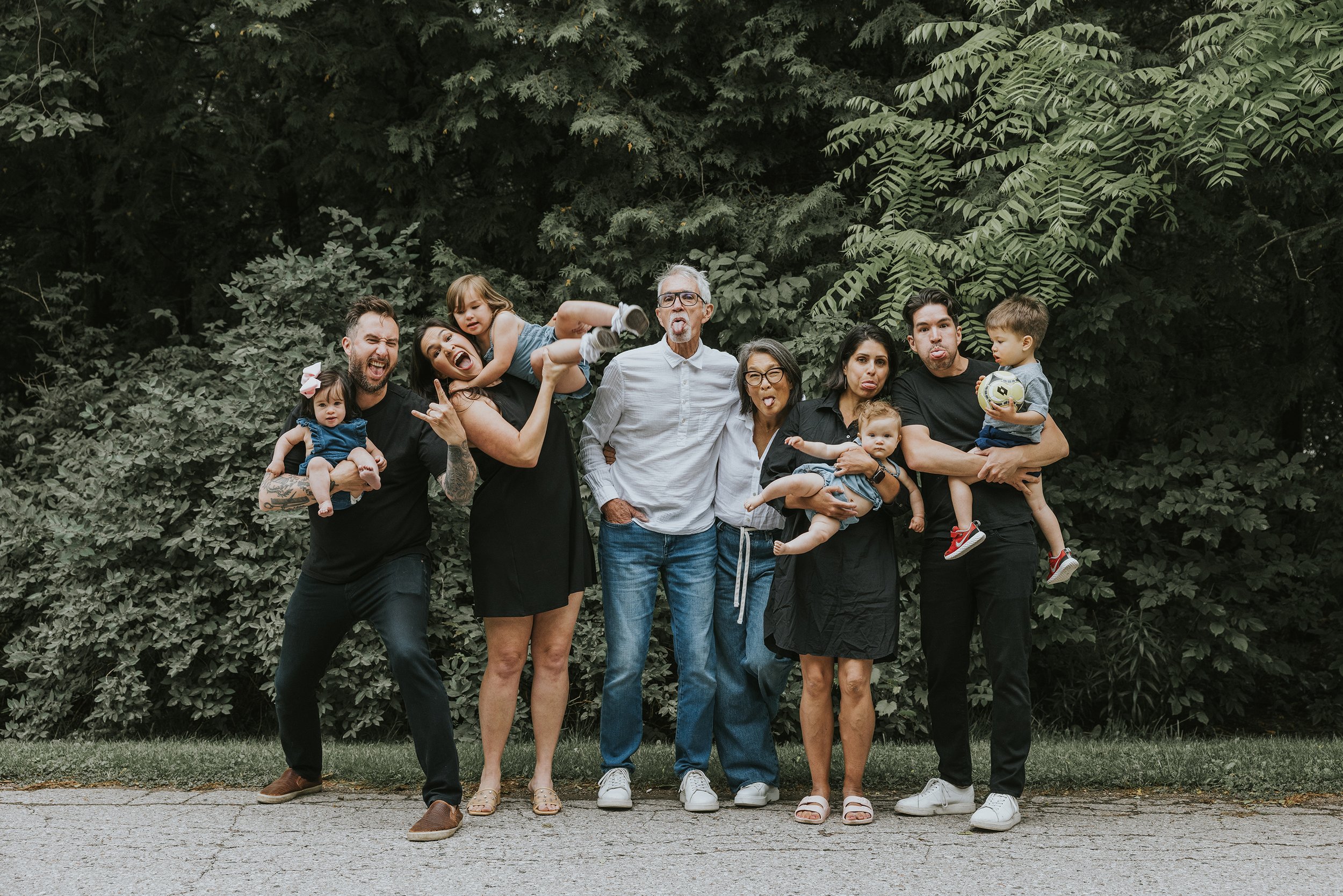 A candid and playful family portrait taken in a park, with everyone making silly faces.