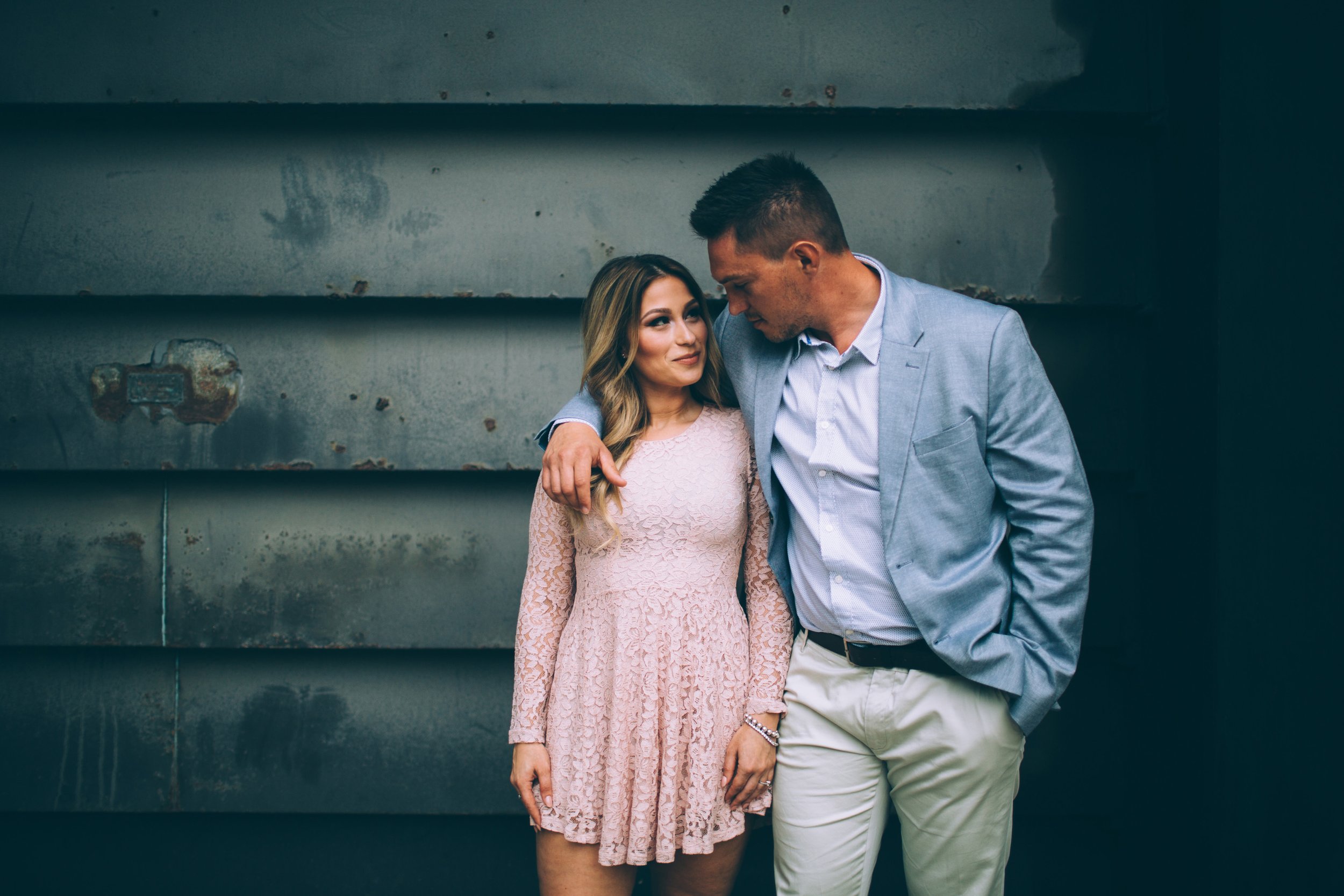 A couple embracing in front of a weathered urban wall, creating a romantic and edgy vibe.