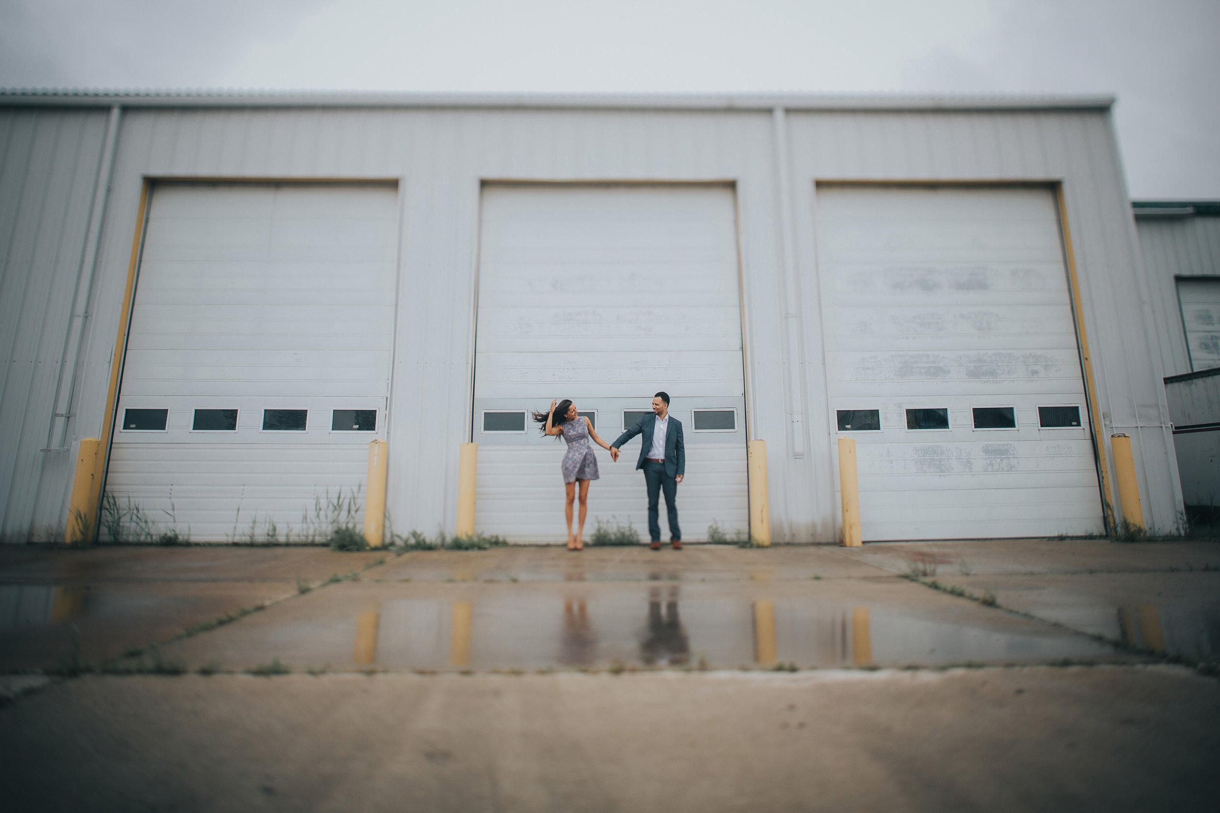 A couple holds hands in front of an industrial building, symbolizing their urban romance.