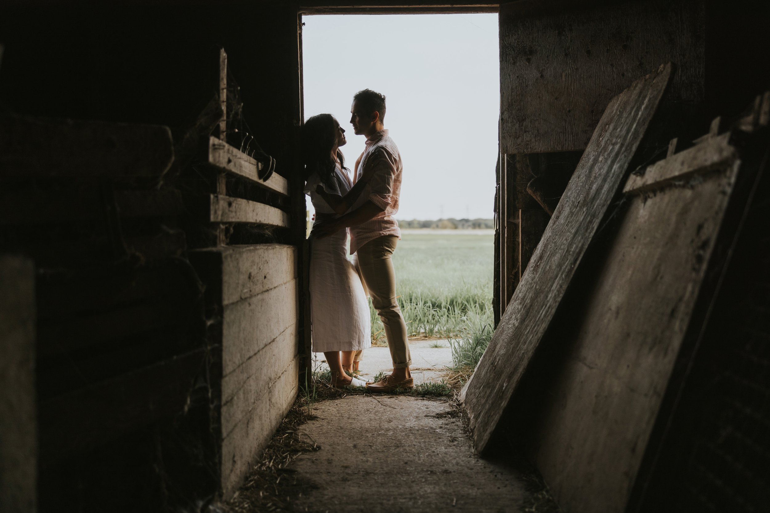 Couple standing in the doorway of a barn, silhouetted against the light, creating a romantic and rustic engagement photo.