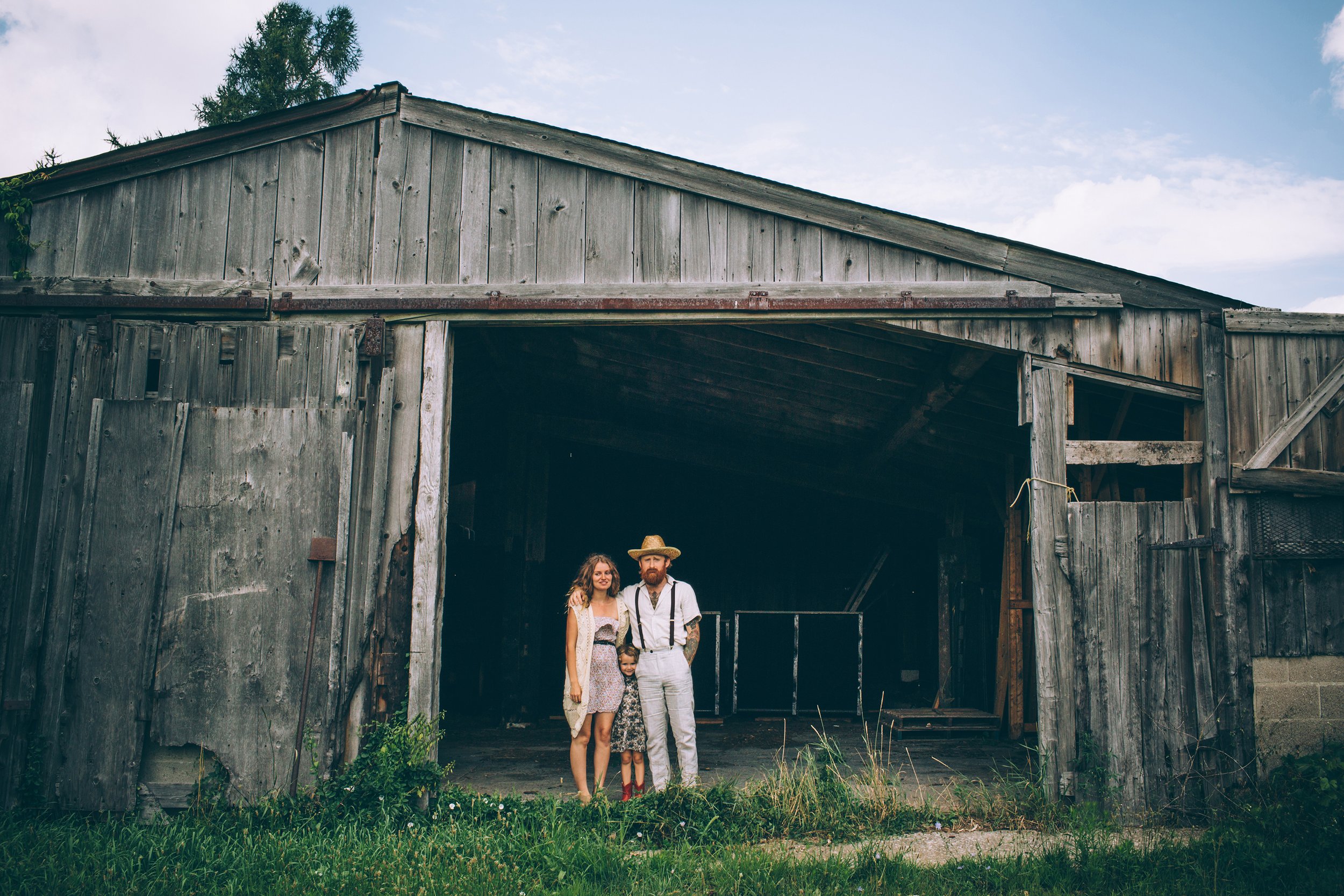 A family standing together in front of a weathered barn, dressed in rustic attire, creating a country-inspired portrait.