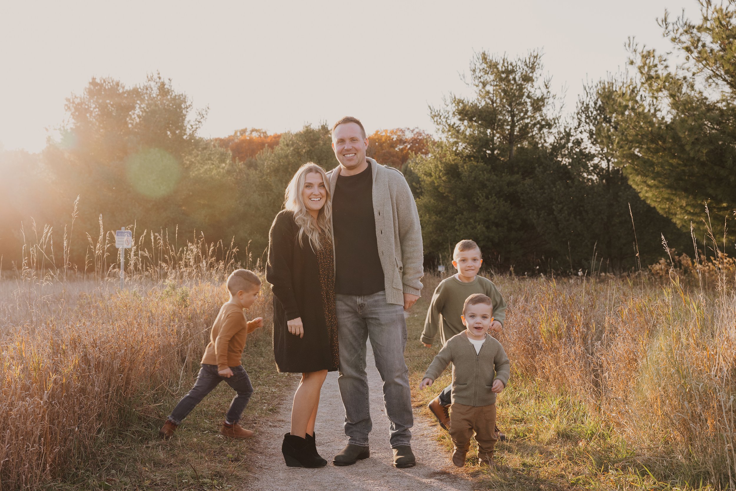 A family of five enjoying a warm sunset in an autumn field, with children playing and parents smiling.