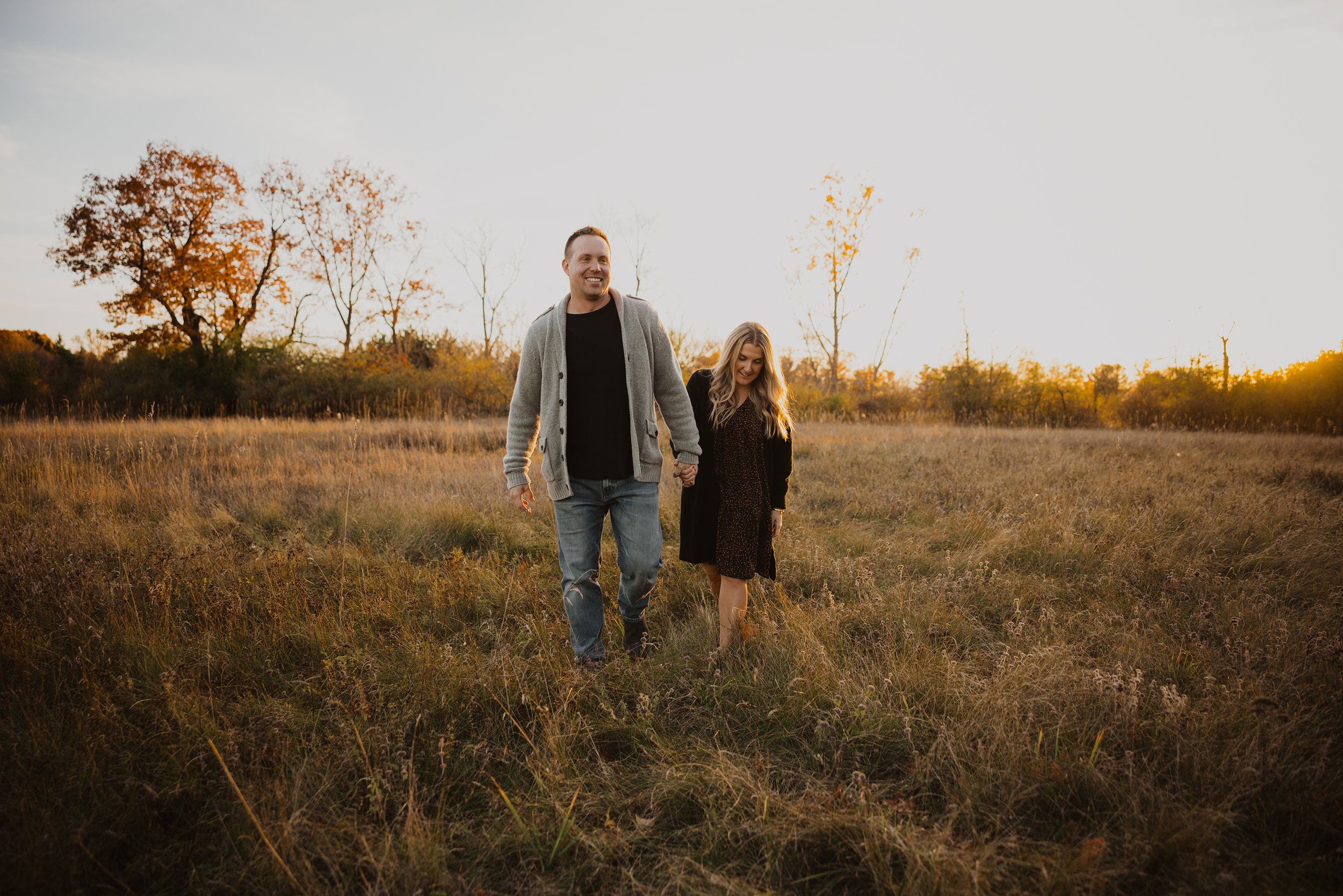 A couple walking hand in hand through a field at sunset during autumn, with warm, golden hues highlighting their connection.