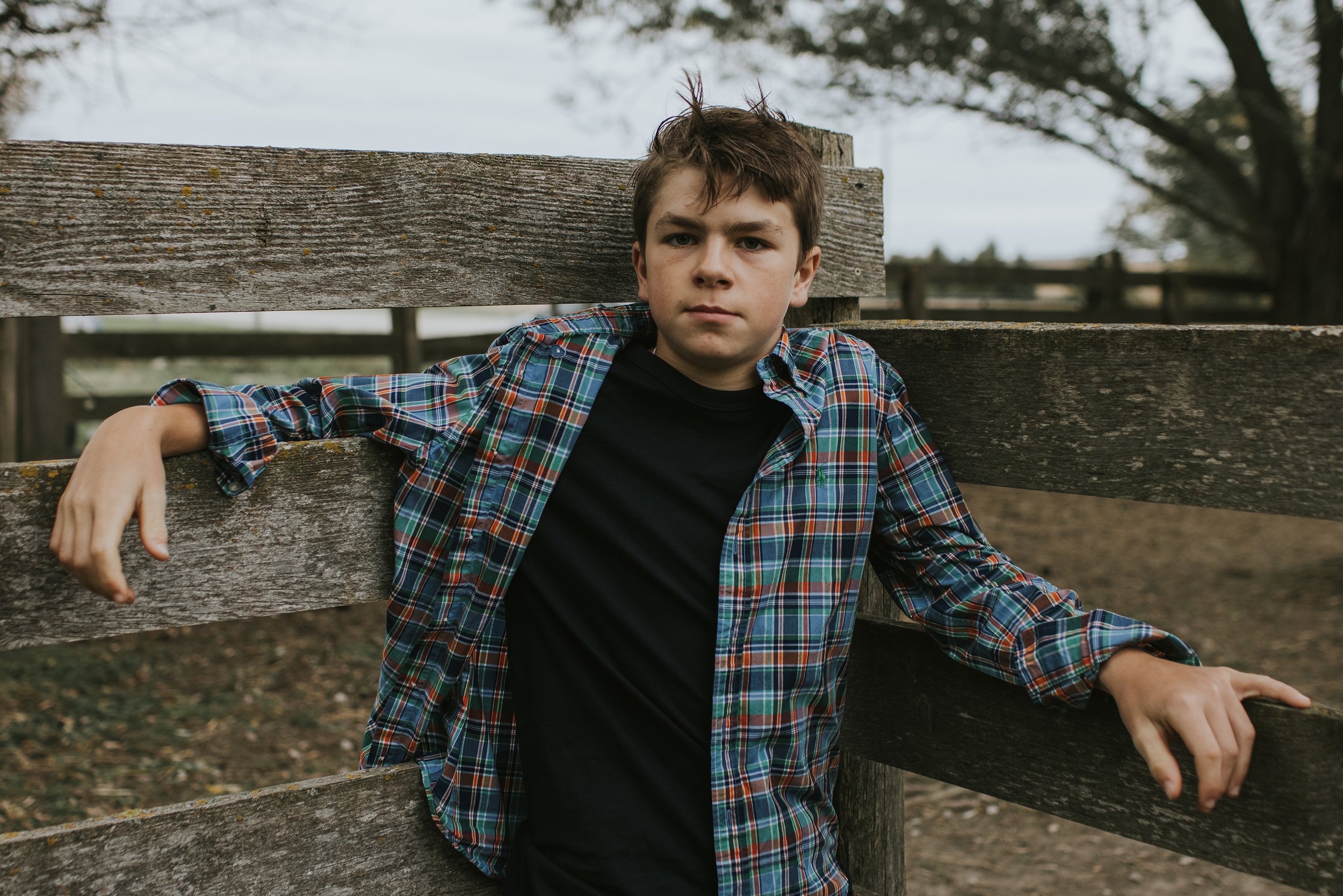 A casual portrait of a teenage boy leaning against a rustic farm fence.