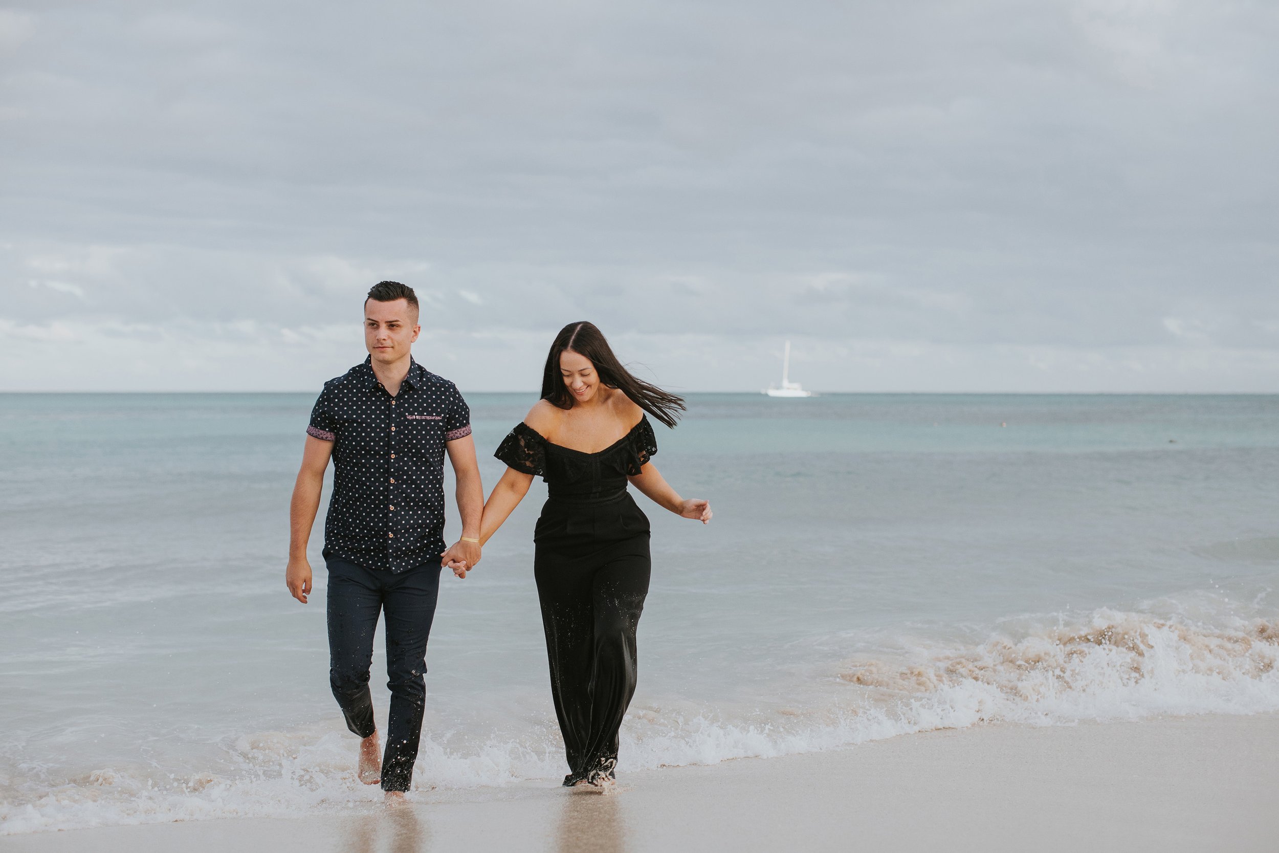 A couple walks hand-in-hand along the shoreline, the ocean waves gently lapping at their feet. The scene exudes a sense of peace and togetherness as they enjoy a tranquil moment by the sea.