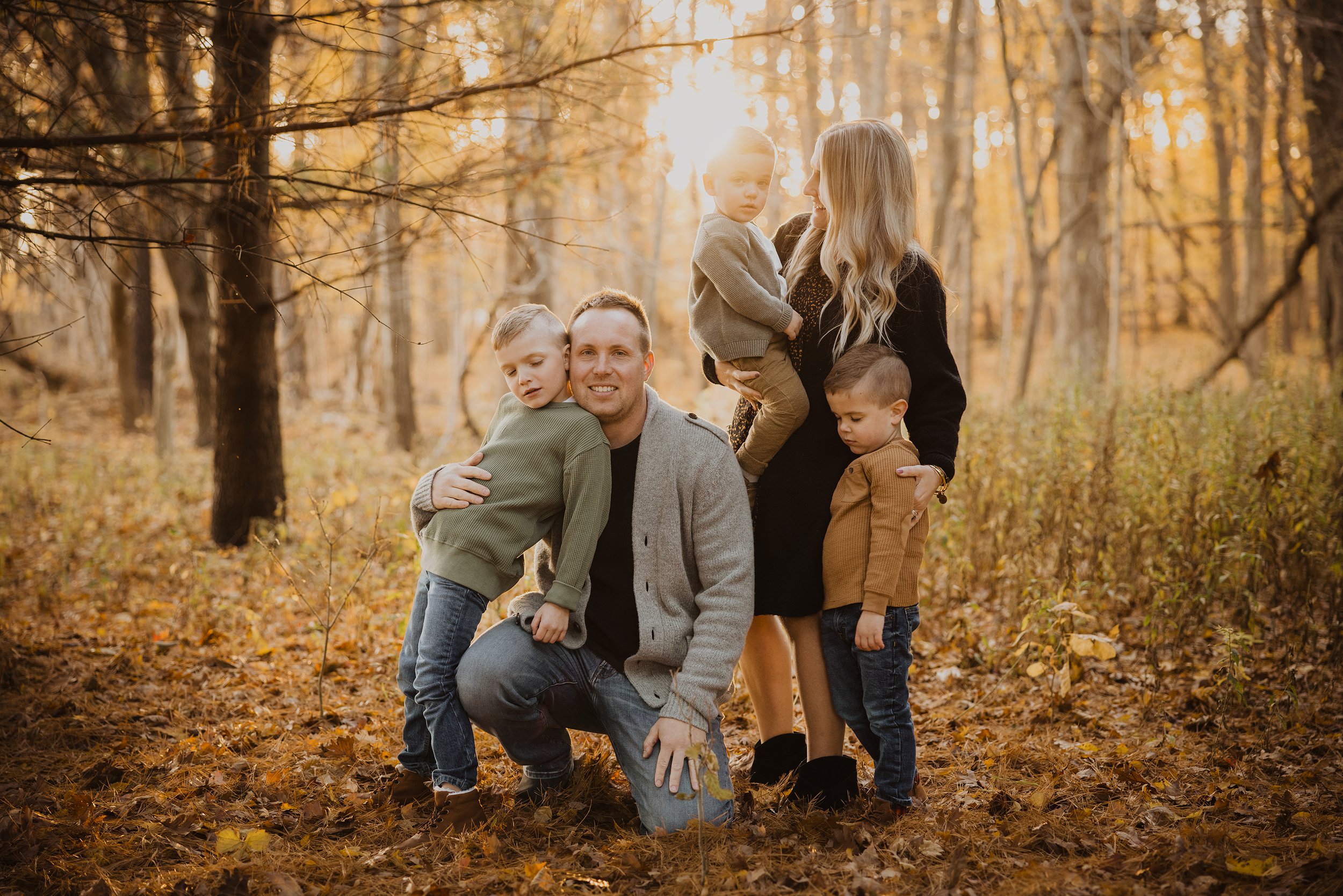A family poses together in an autumn forest, surrounded by golden leaves and soft sunlight, capturing the essence of the season.