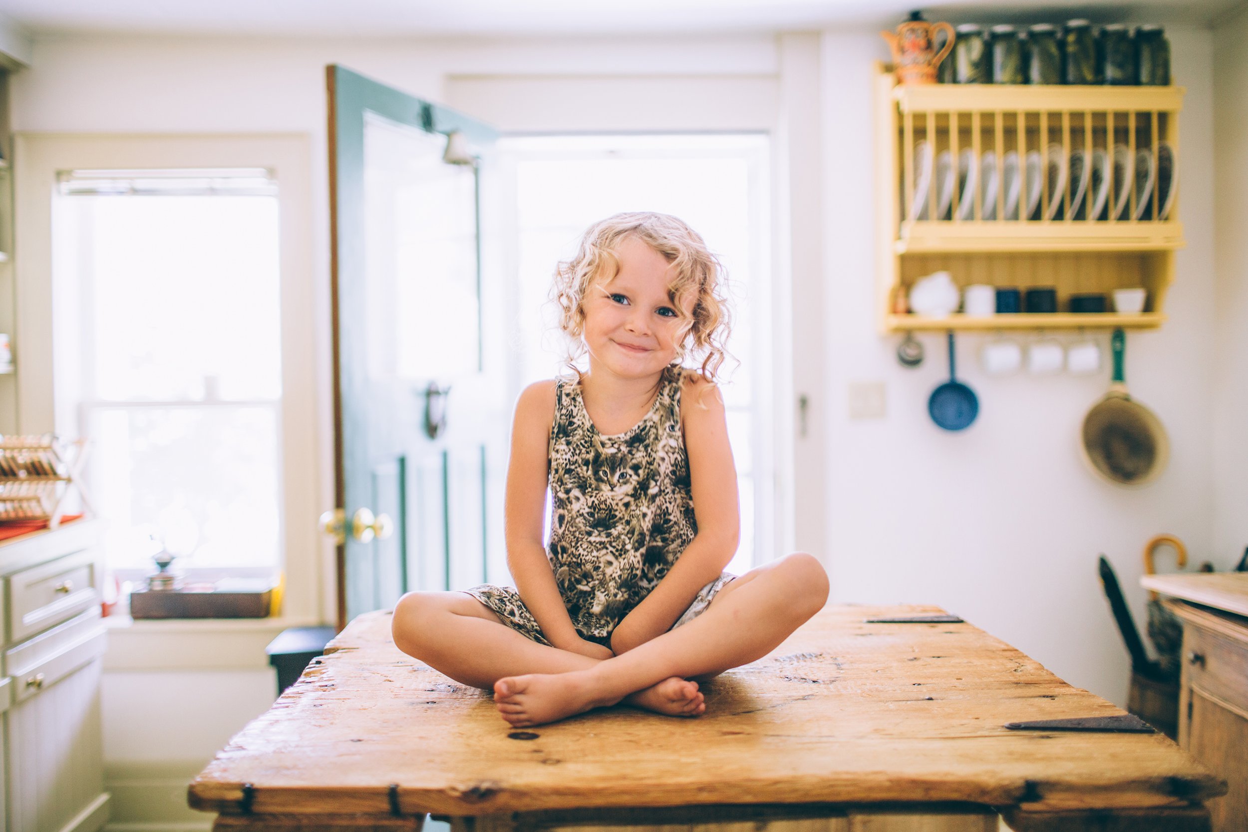 A cheerful girl sitting cross-legged on a wooden kitchen table in a vintage home, radiating warmth and charm in London, Ontario.