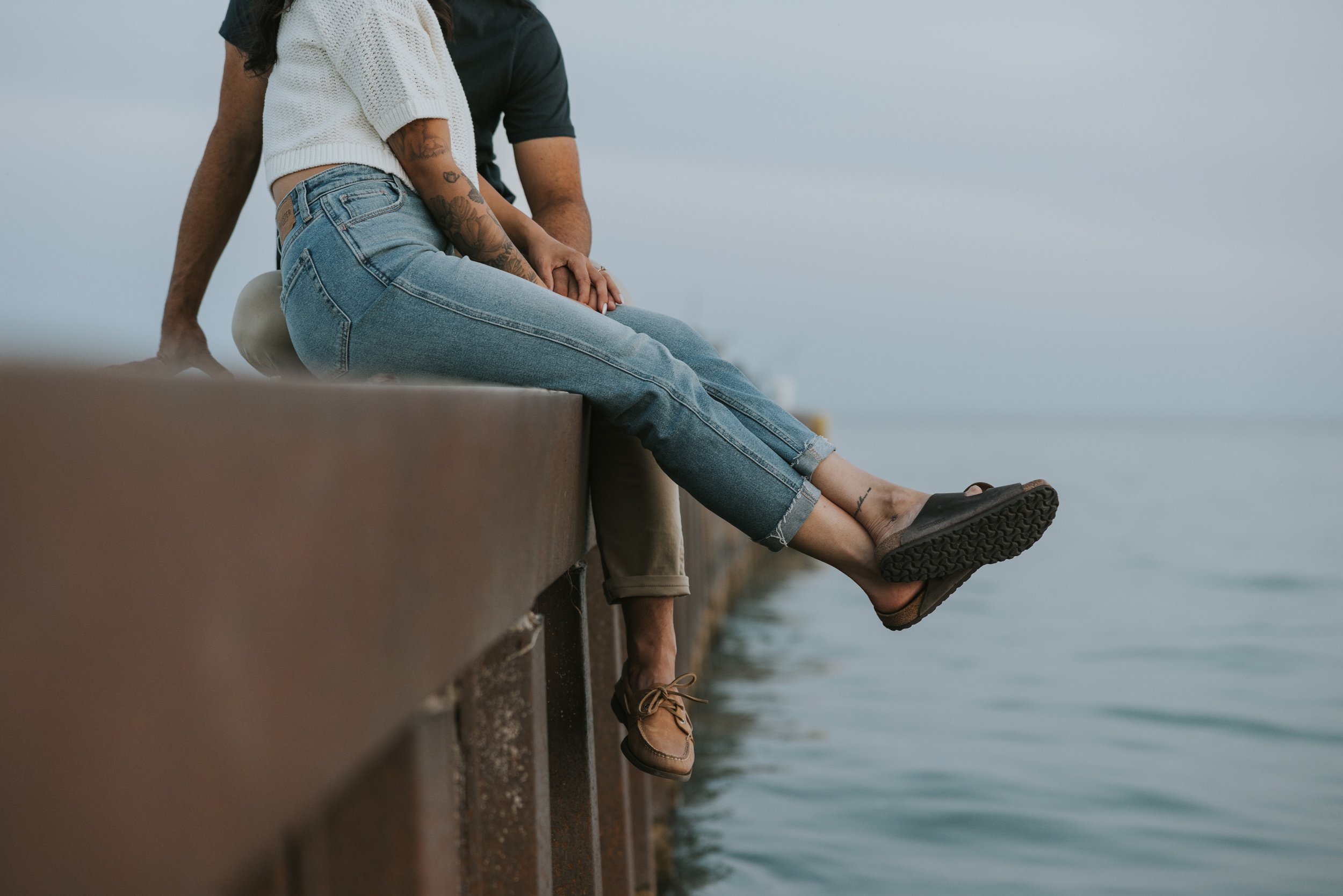 A couple sitting closely together on a beach, their legs dangling over the water as they share a relaxed and intimate moment in nature.