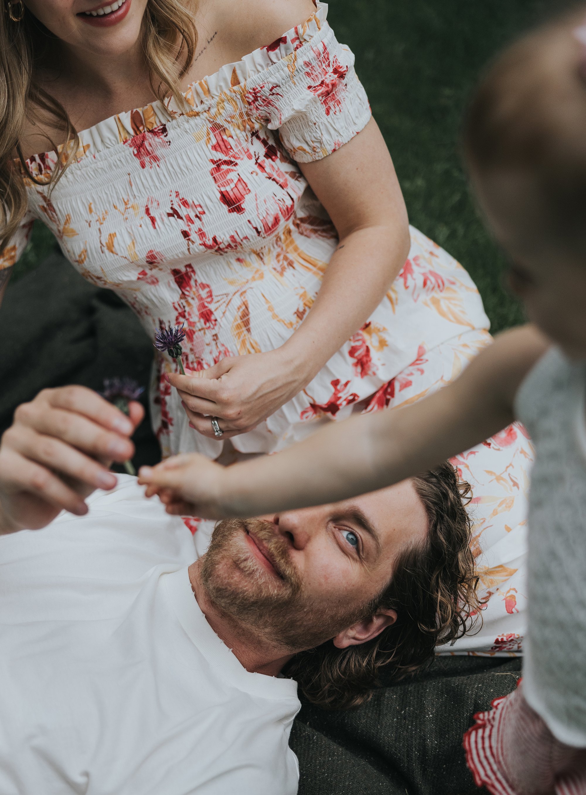 A serene family portrait taken in a lush garden, featuring a woman in a floral dress, radiating warmth and love.