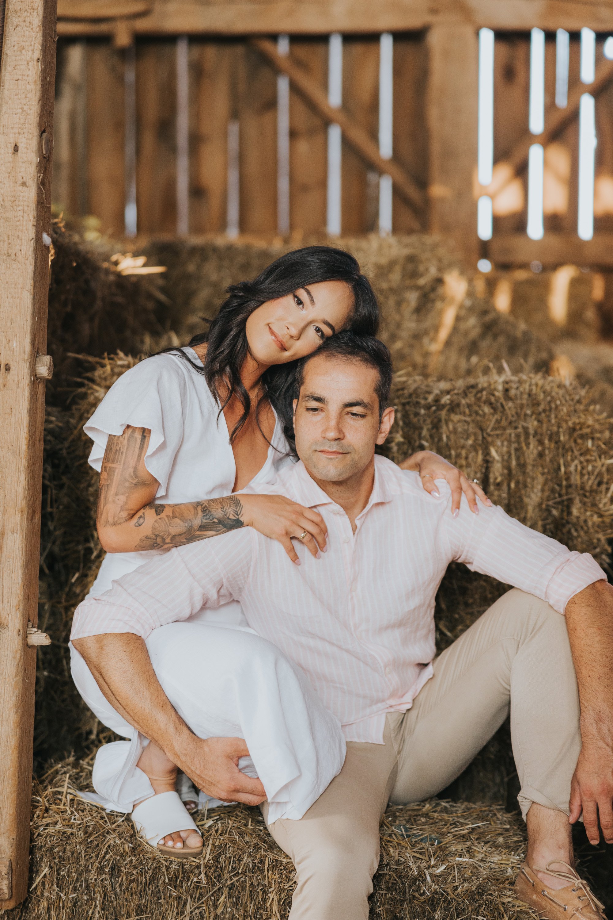 A couple sitting intimately on hay bales inside a rustic barn, enjoying a quiet moment during their engagement session.