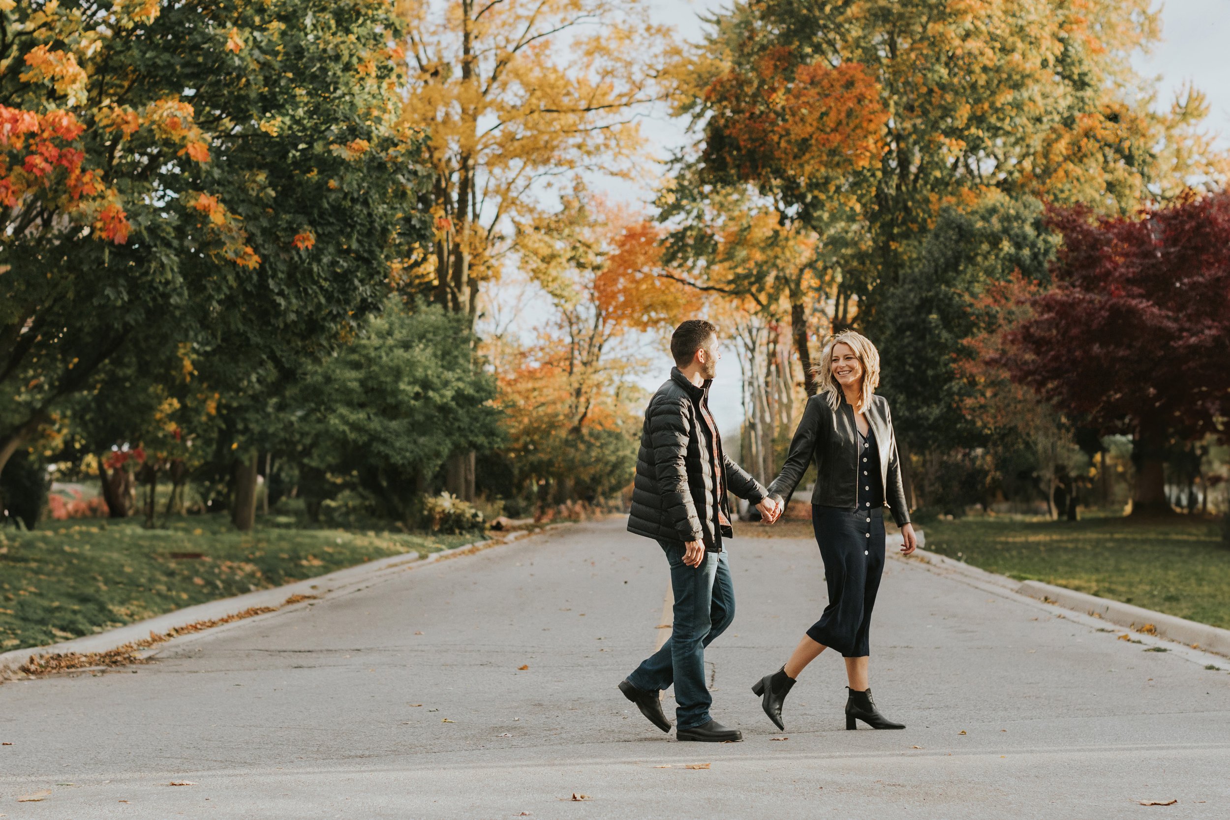 A couple walks hand in hand through a park adorned with vibrant autumn leaves, enjoying their engagement session surrounded by the beauty of the season.