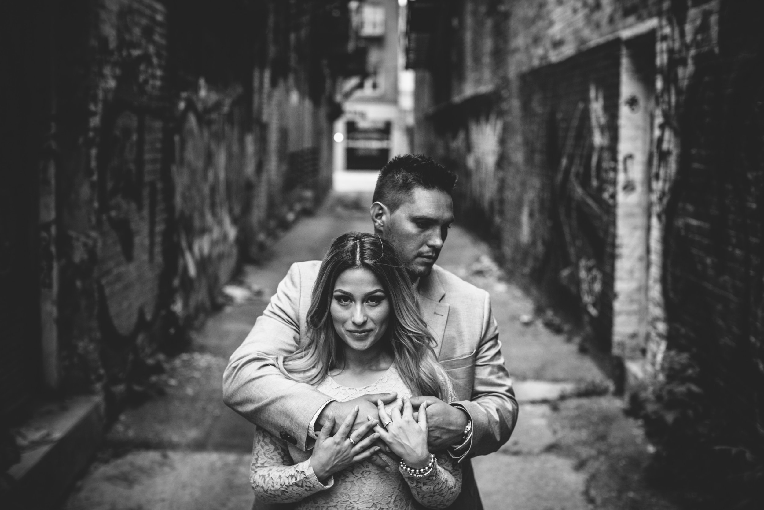 Black and white photo of a couple embracing in a narrow urban alleyway, with a gritty, intimate atmosphere.