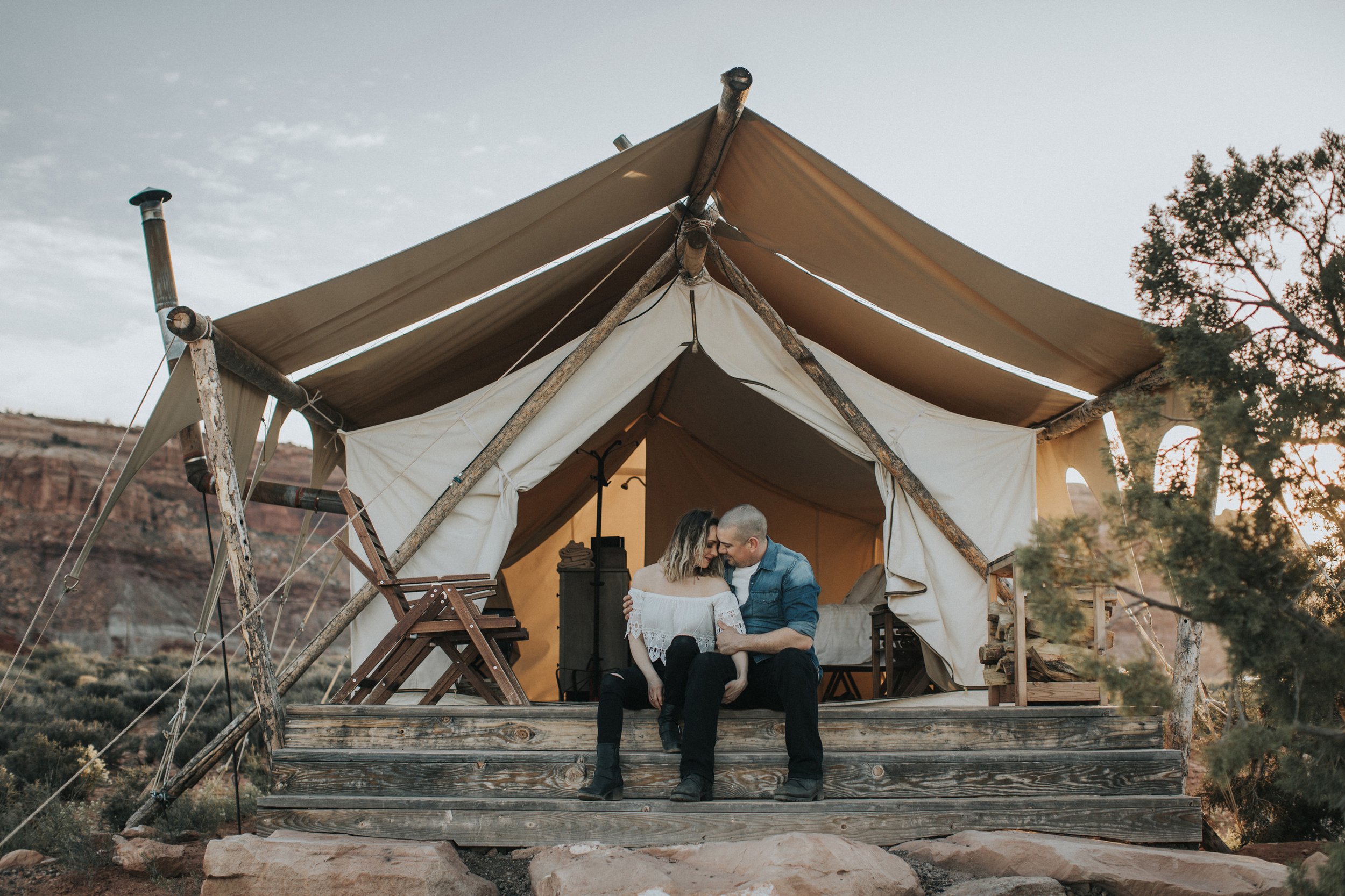 A couple cuddles on the front porch of a tent, surrounded by nature.