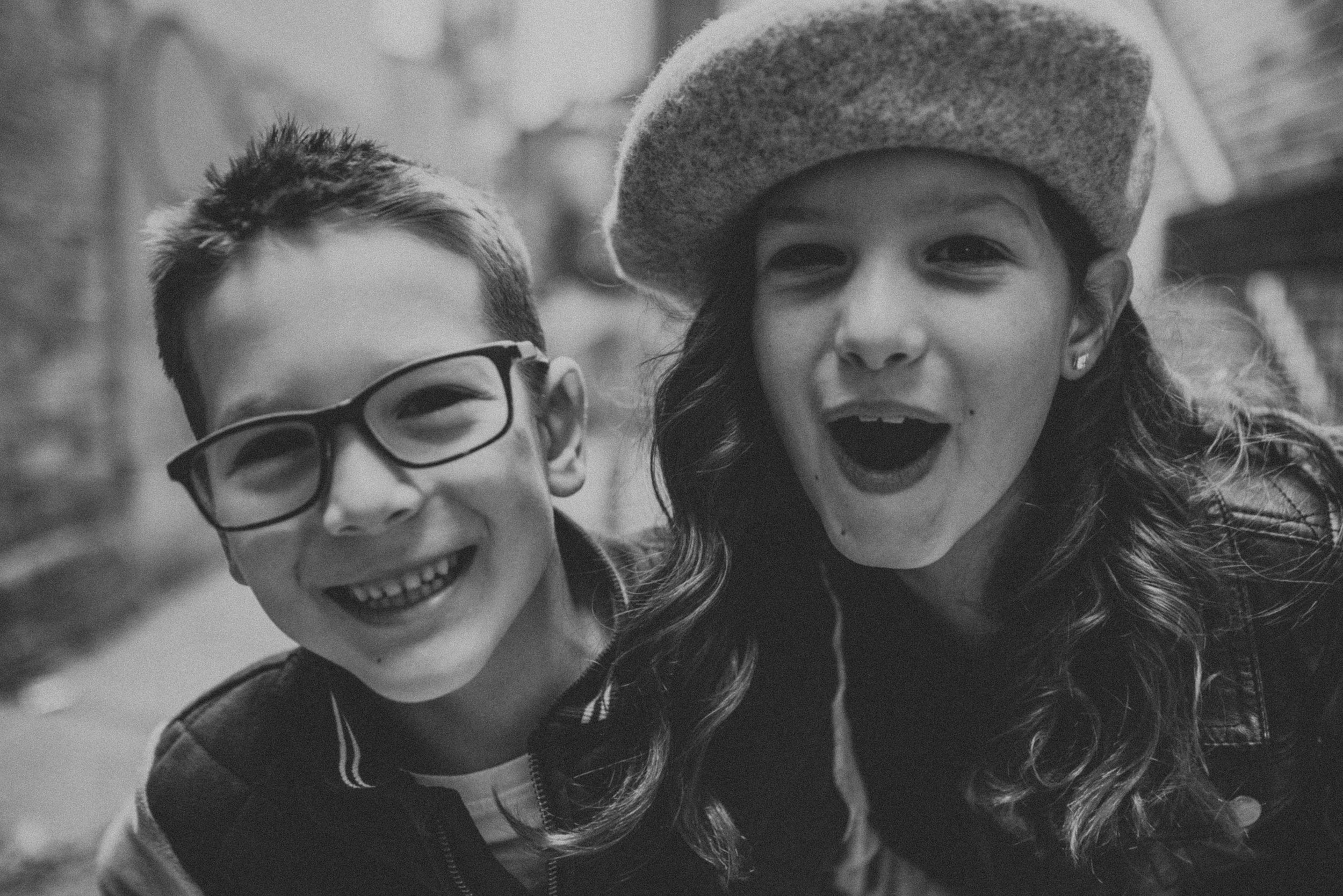 Siblings Laughing Closeup Berets Glasses Black White: A black-and-white closeup of two siblings smiling, one wearing glasses and the other a beret.