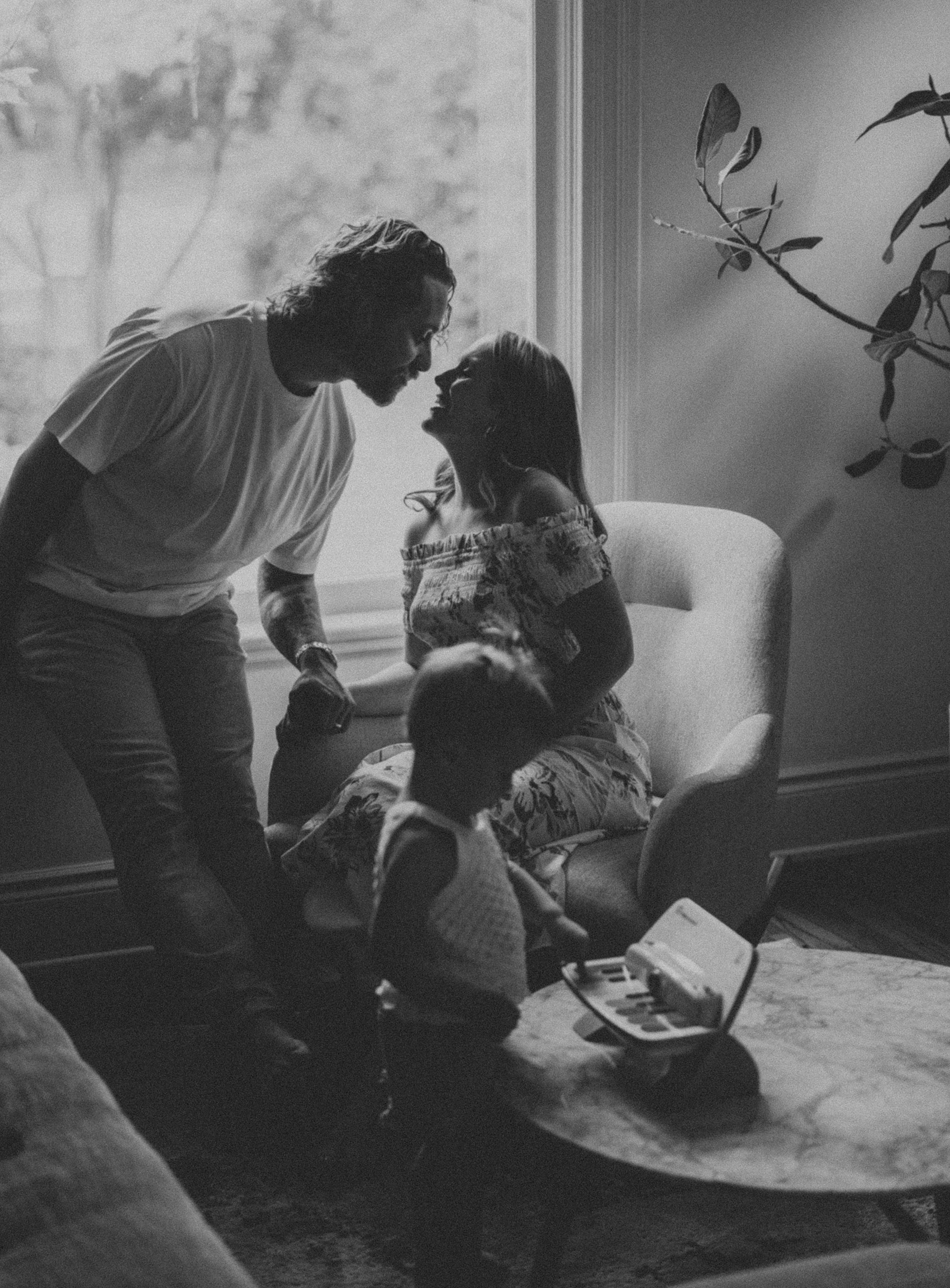 A tender indoor scene of a family where the parents are sharing a loving moment while their young child plays nearby, capturing a candid connection.