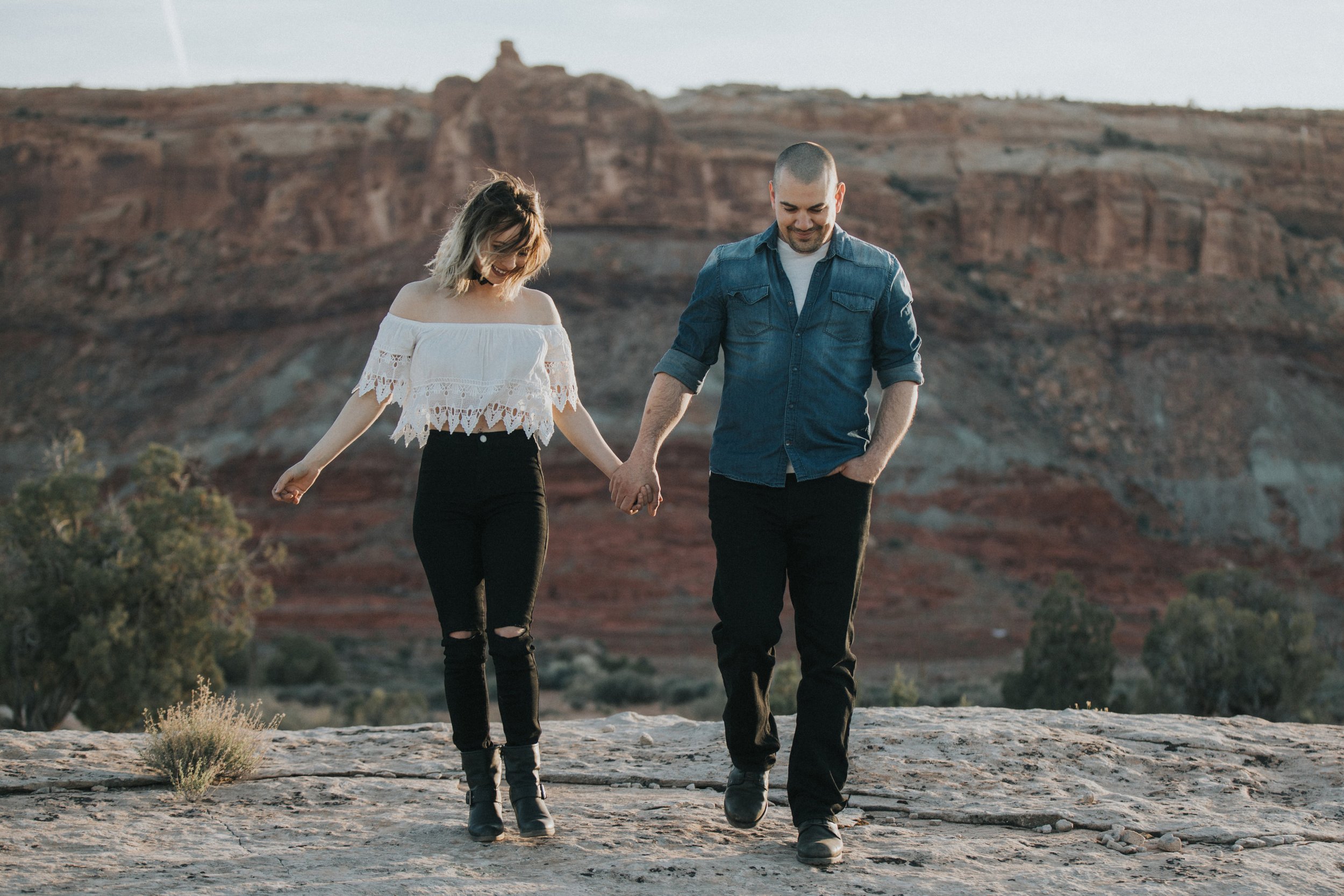 A couple walks hand in hand through a canyon at sunset, enjoying the natural beauty of the rugged landscape.