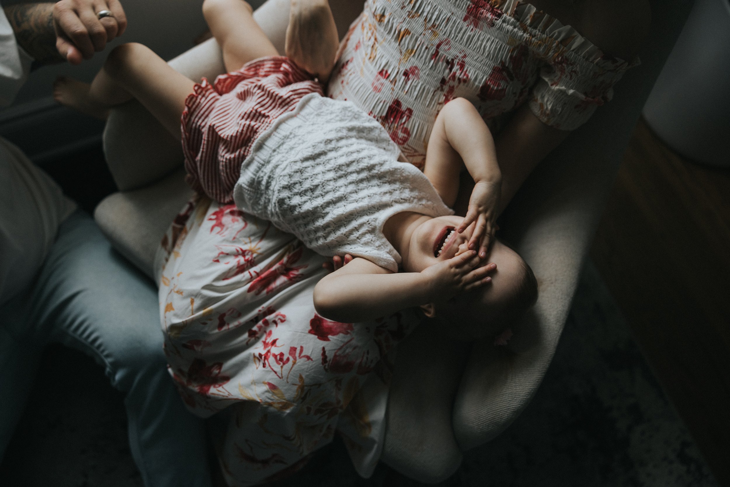 A joyful child laughing while laying on a parent's lap, dressed in red and white, with the parent's arms gently holding them.