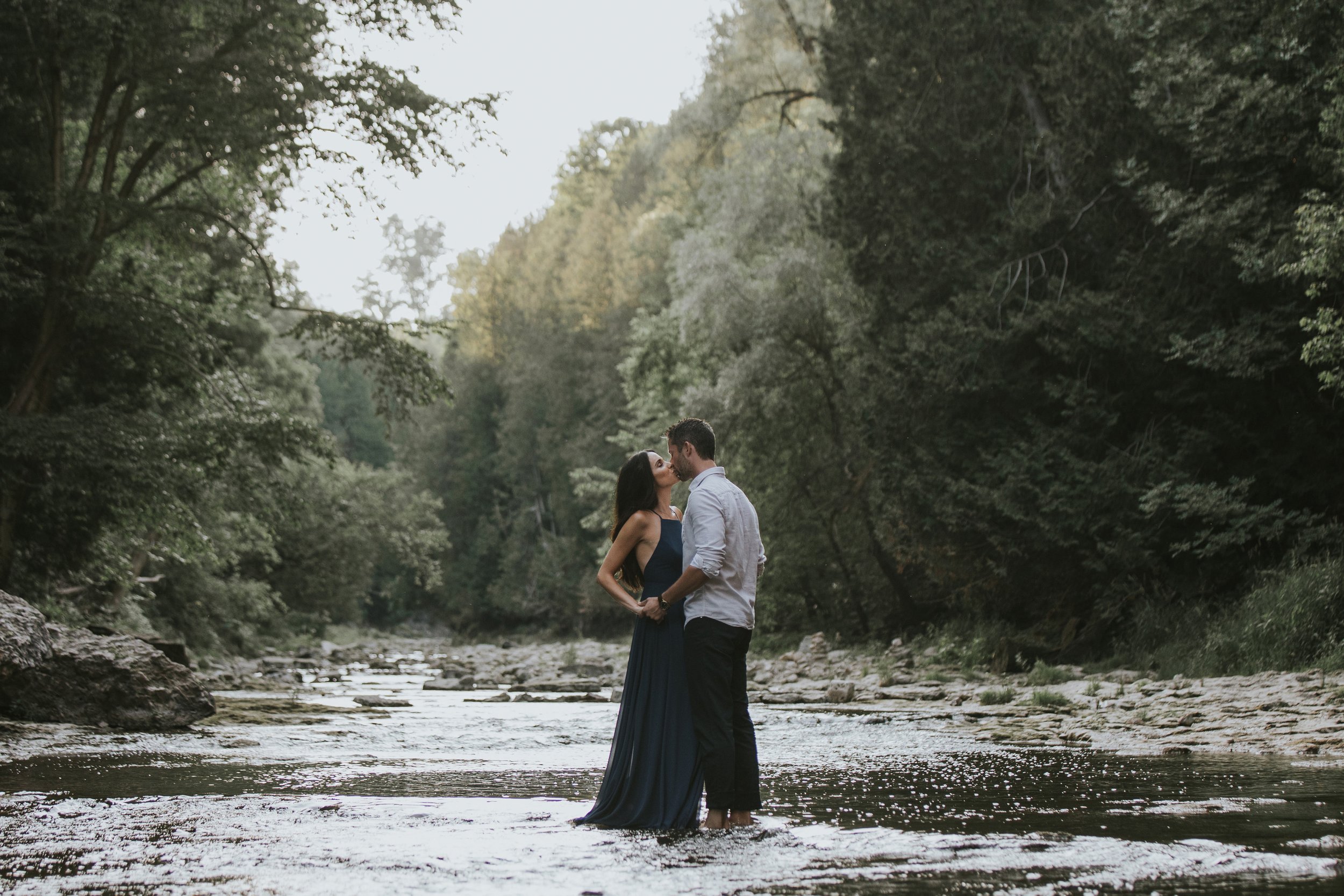 A couple walks barefoot through the shallow waters of a river in the scenic Elora Gorge, sharing an intimate moment surrounded by nature.