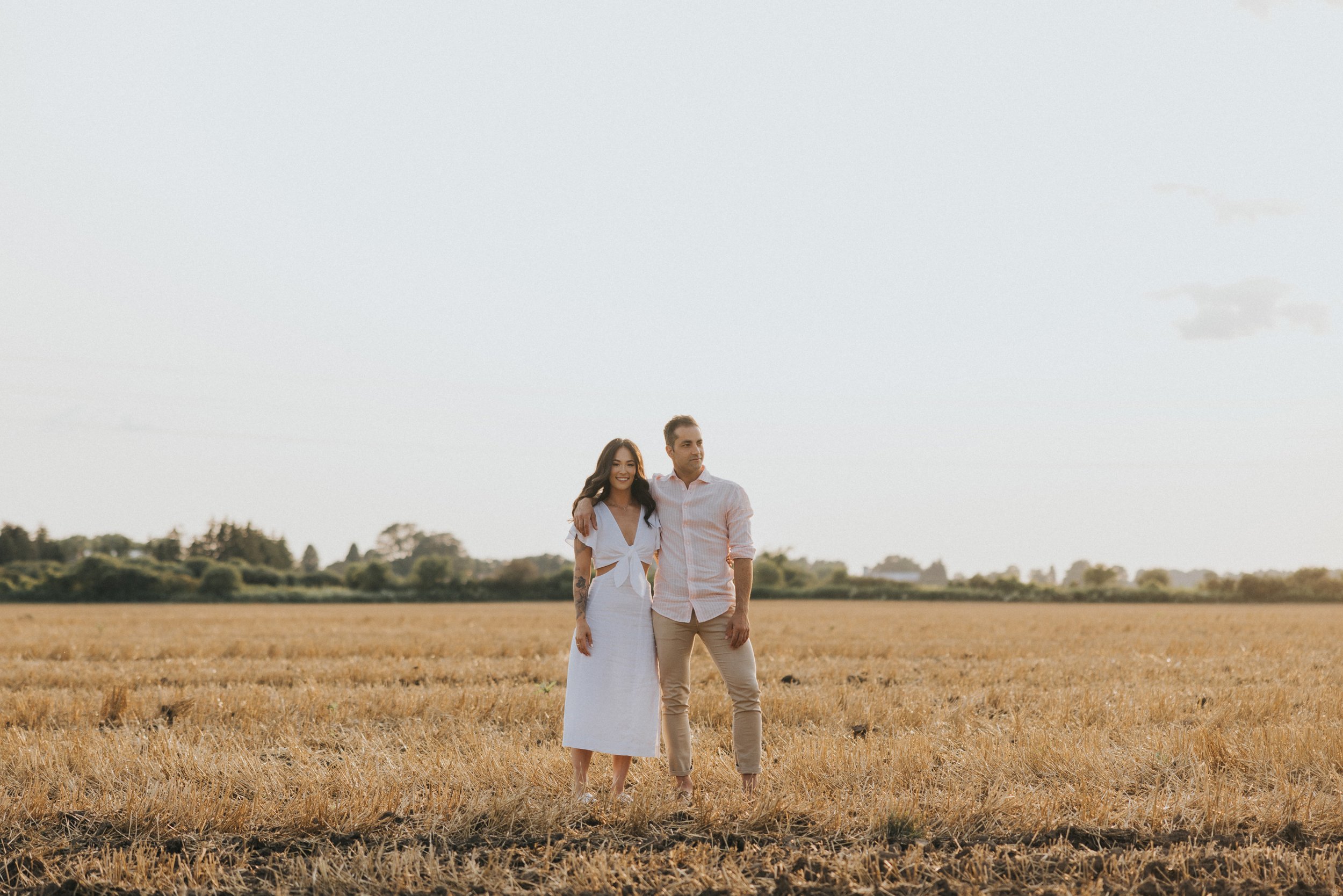 A couple standing together in a golden field during sunset, sharing a loving moment.