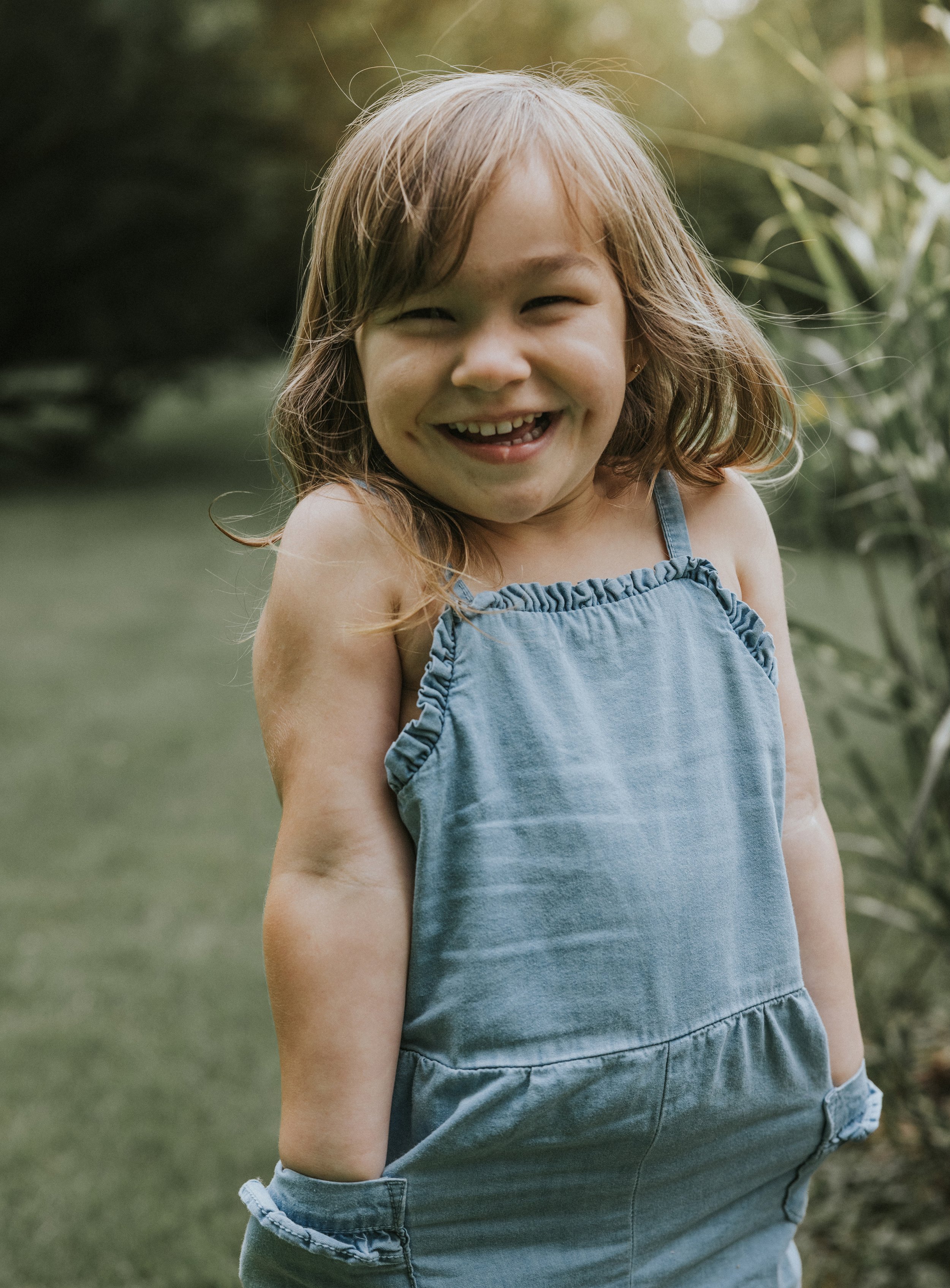 A cheerful girl smiling outdoors in Bayfield, Ontario, during summer, with greenery in the background.