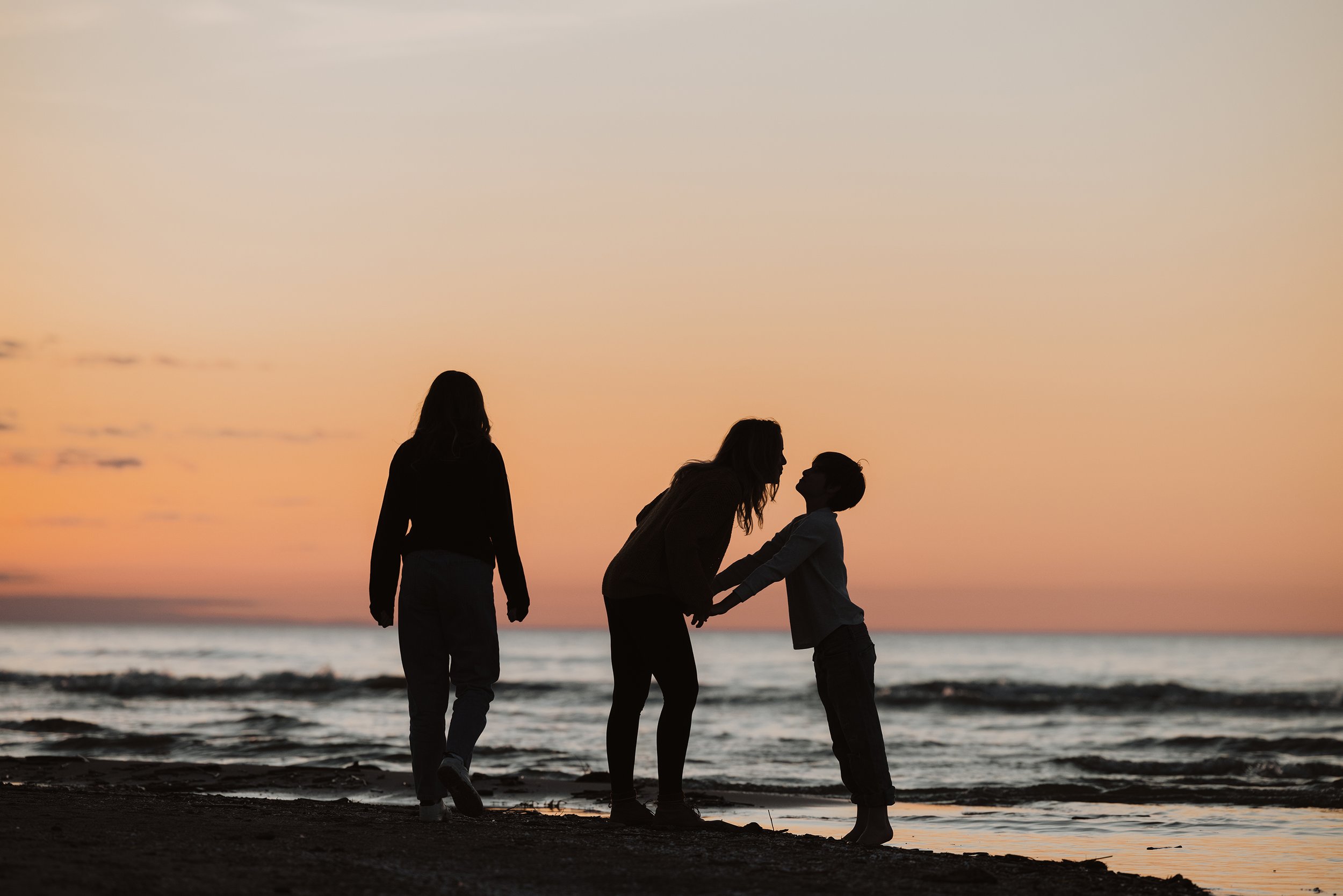 A family enjoying a walk on the beach at sunset, with silhouettes against a vibrant sky.