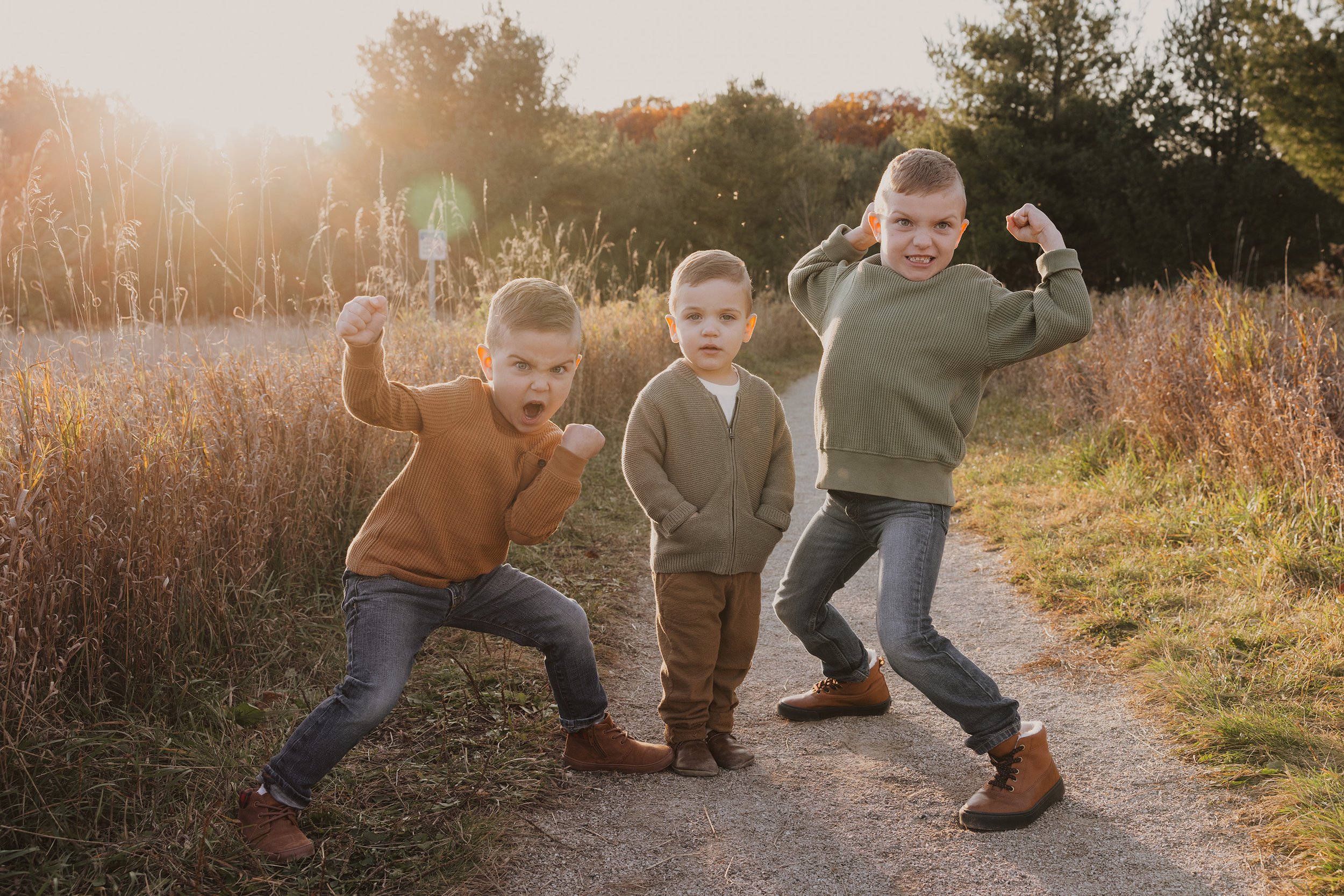 Three brothers striking playful poses during a sunset outdoor session, with golden light illuminating the scene.