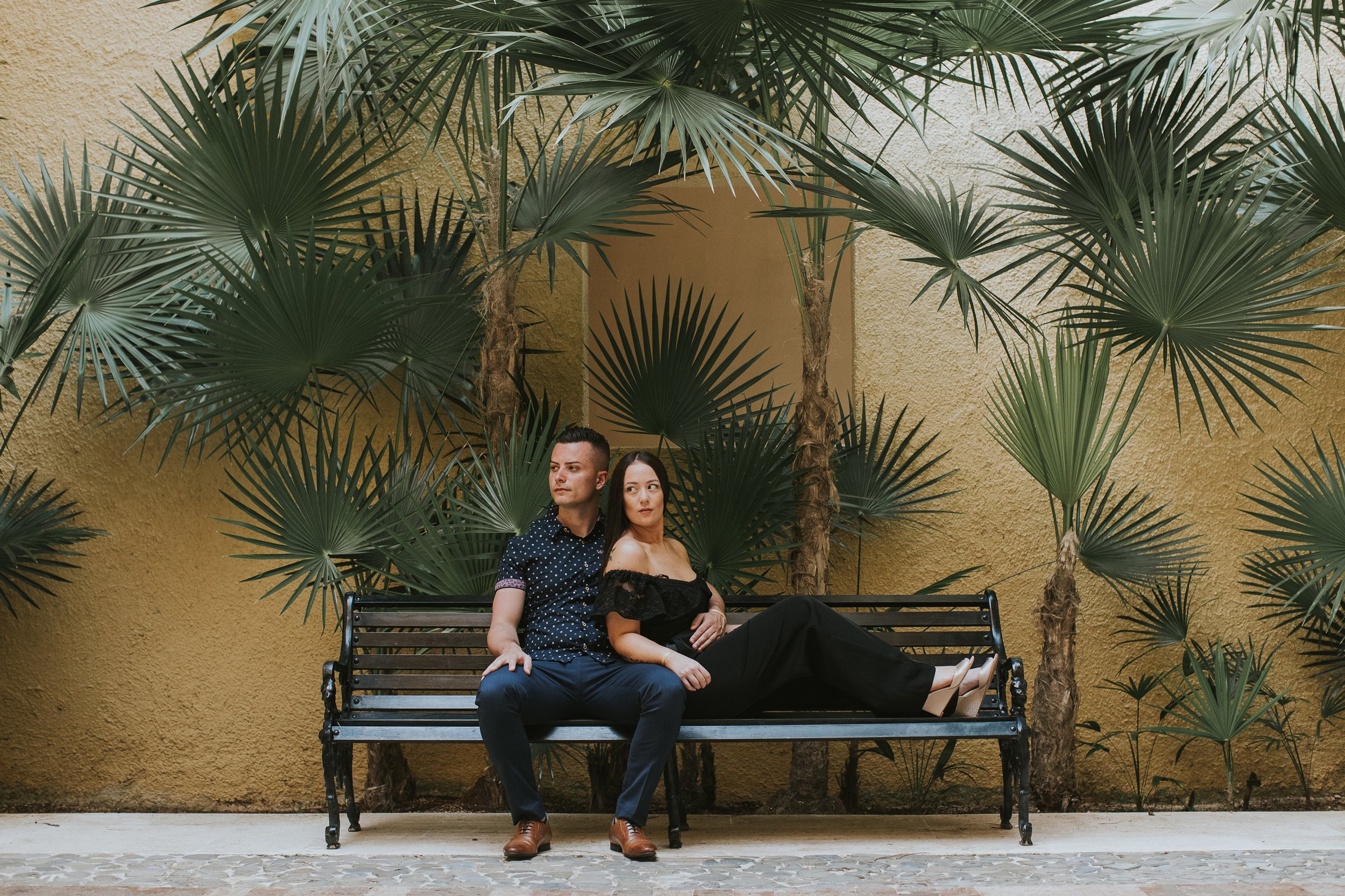 A couple relaxes on a bench surrounded by tropical palm trees, creating a serene and intimate atmosphere as they enjoy each other's company.