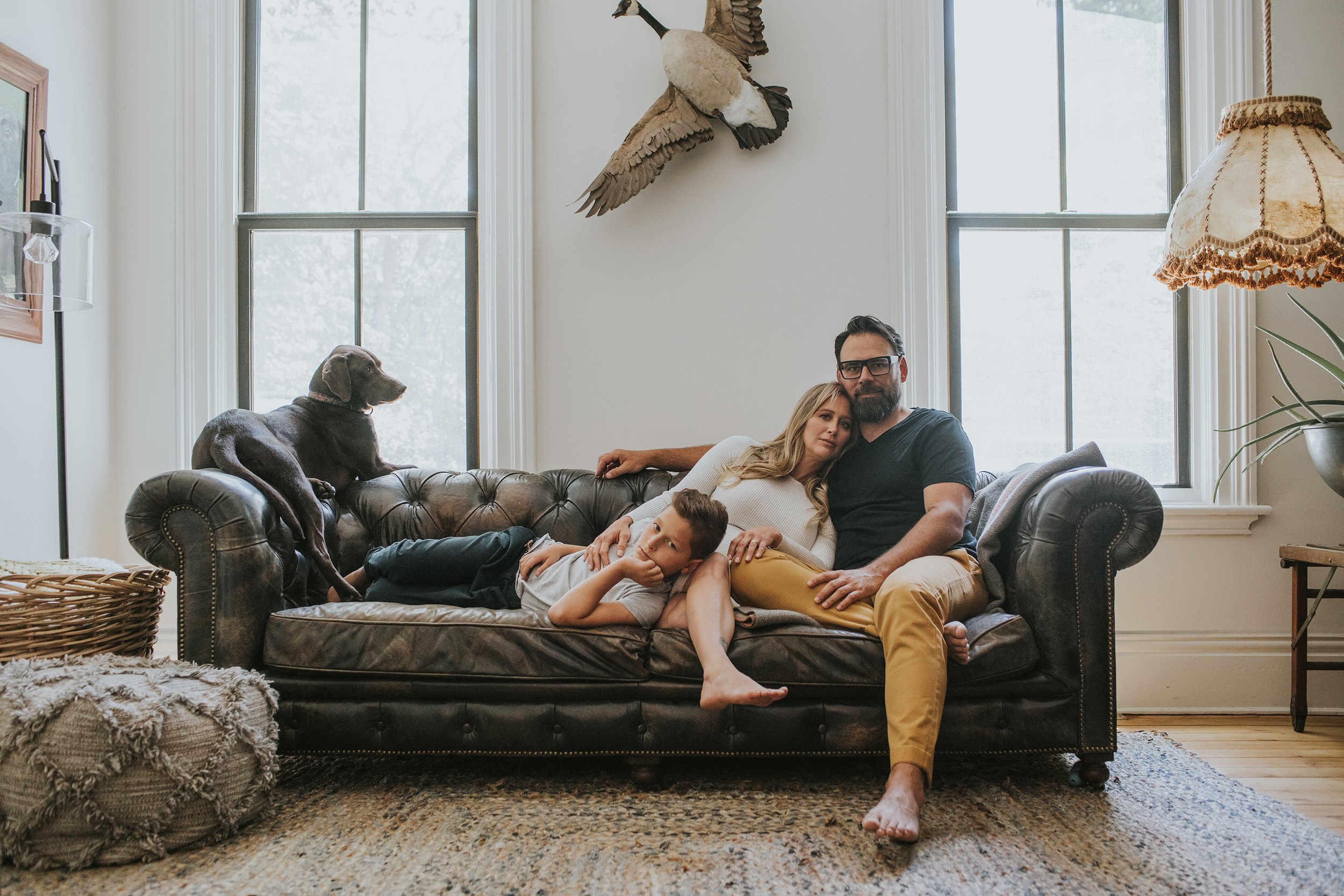 A family lounging comfortably on a leather couch in their cozy living room, with their dog resting nearby, portraying a relaxed and homely atmosphere.