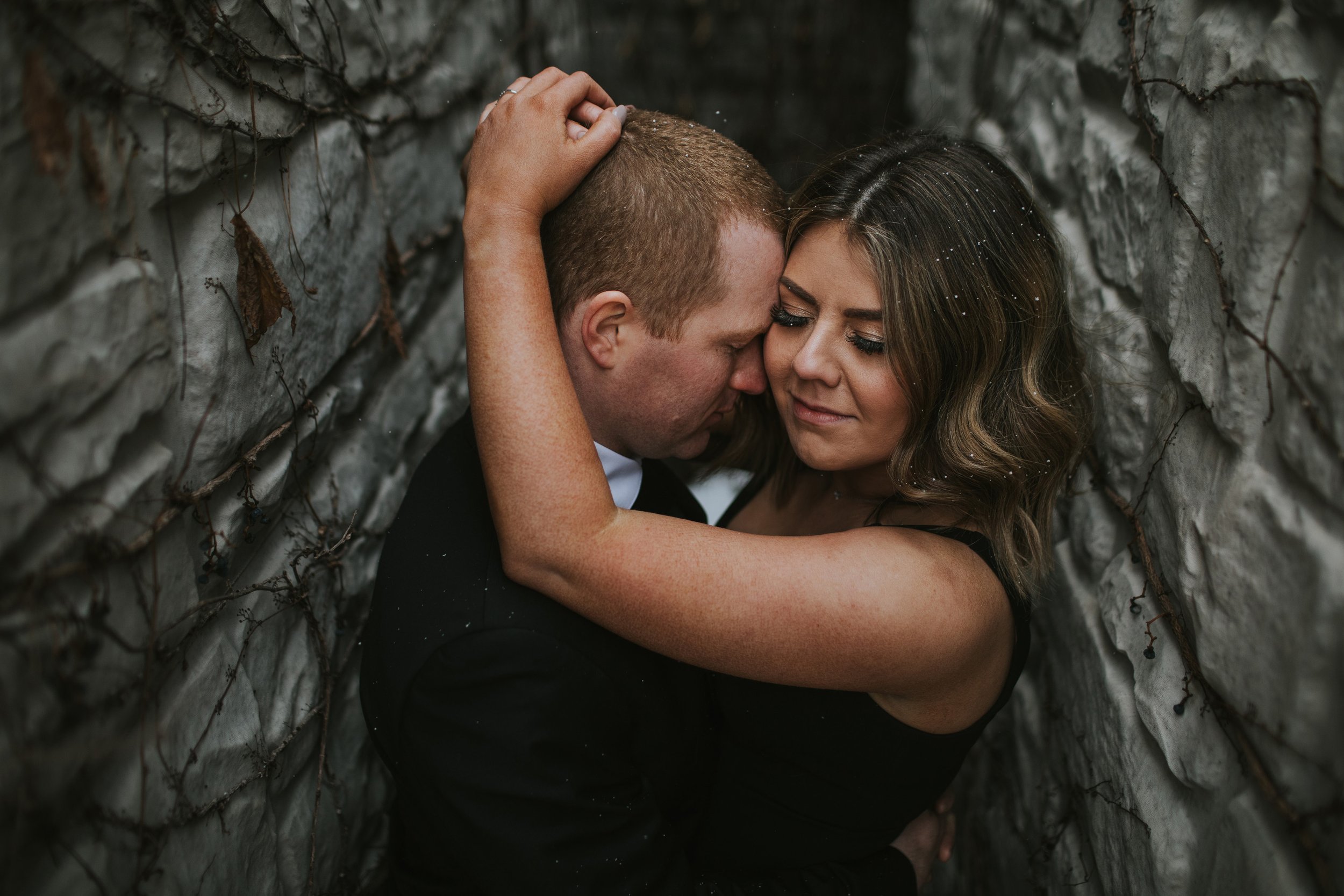 A couple sharing a close embrace in a rustic alleyway, surrounded by stone walls.