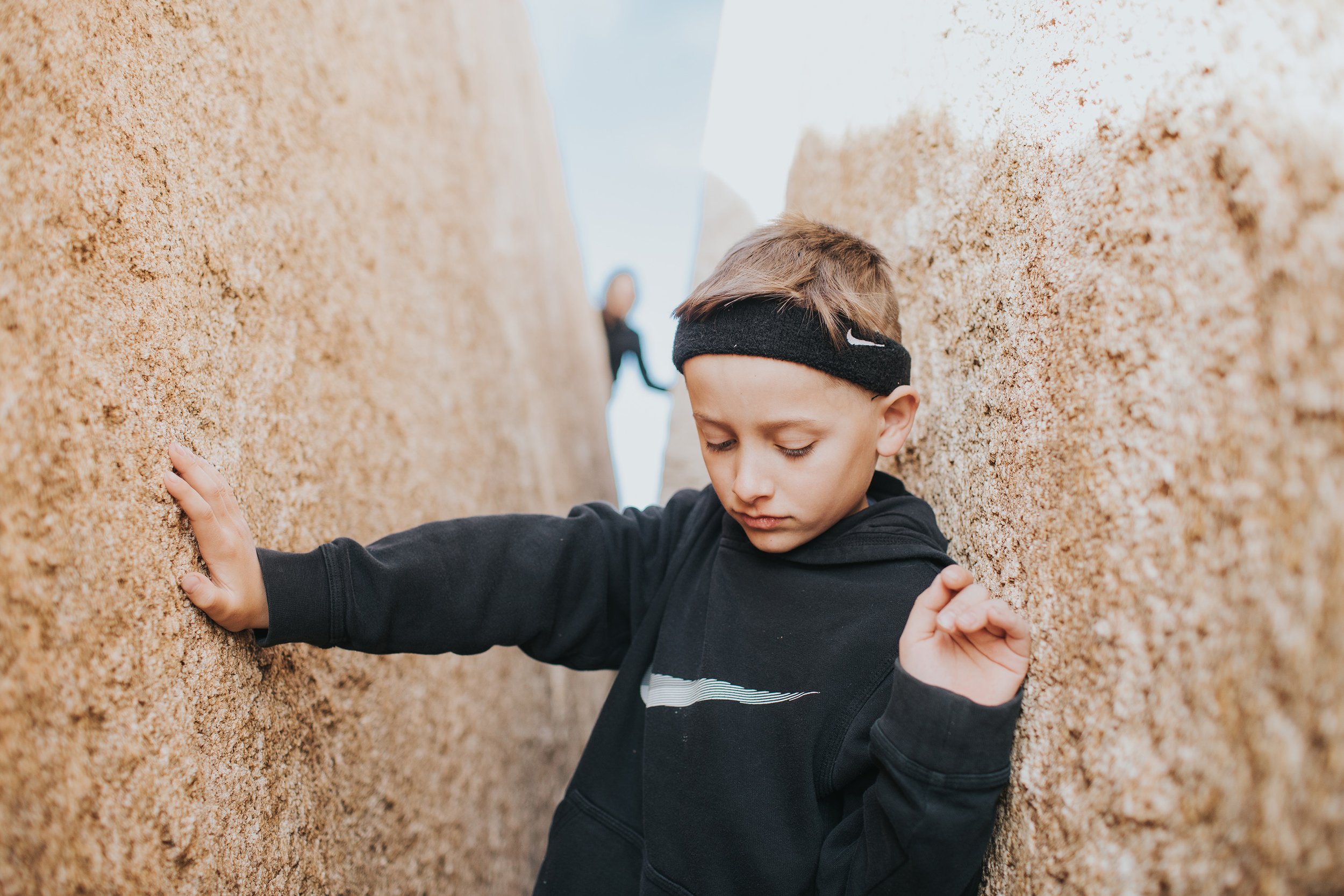 A child adventuring between large rocks, focused and exploring the natural outdoor surroundings.