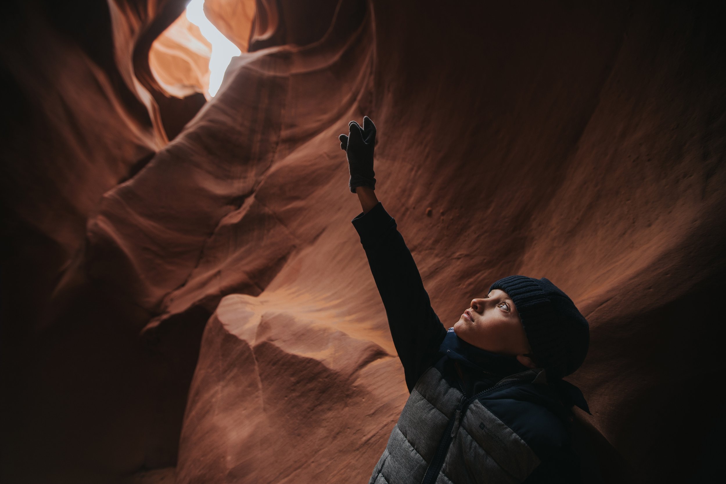 A young boy in a dark jacket and beanie points upward inside a dimly lit cave, capturing a moment of wonder and exploration.