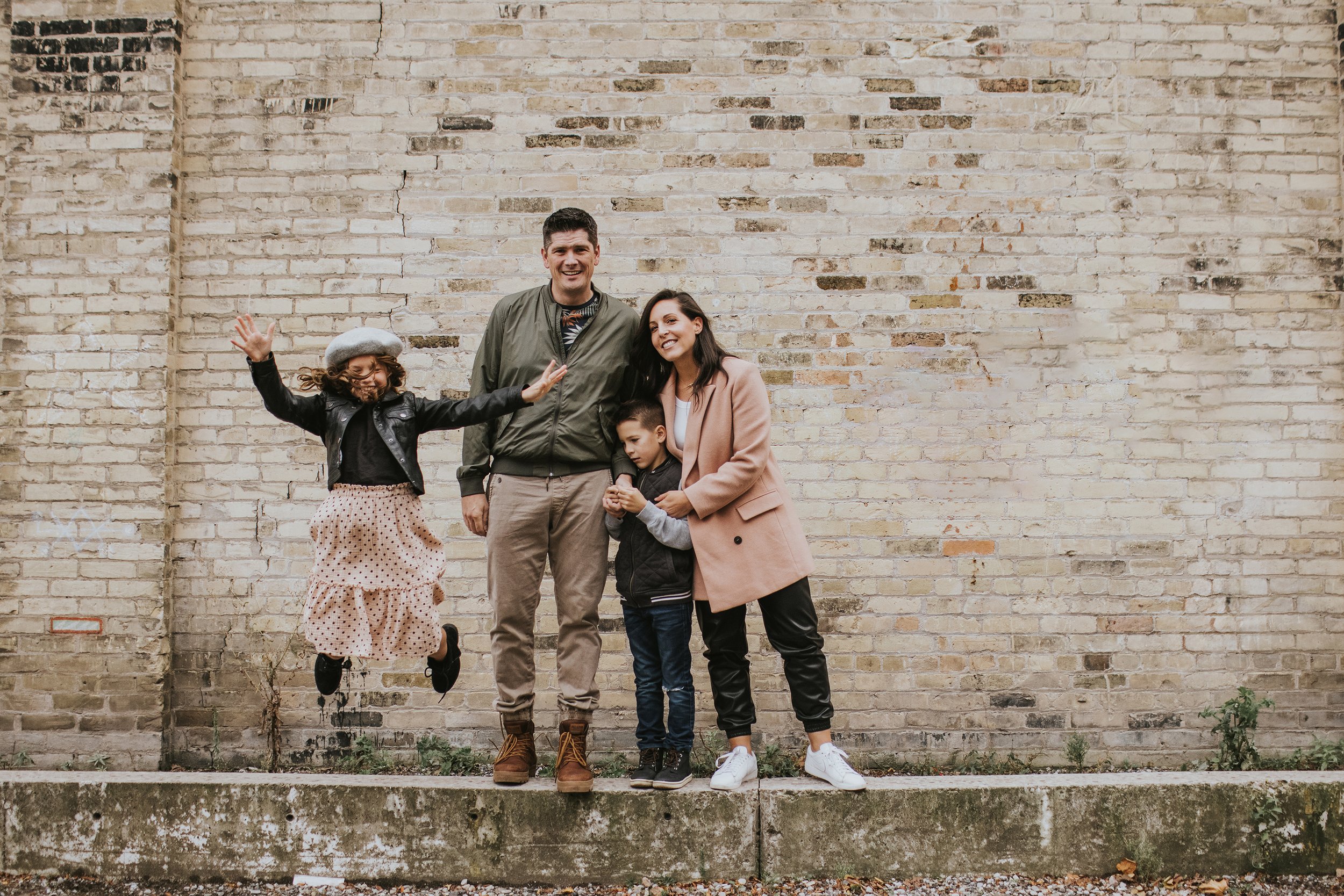 A joyful family photo with a backdrop of a rustic brick wall, highlighting the urban charm of London, Ontario.