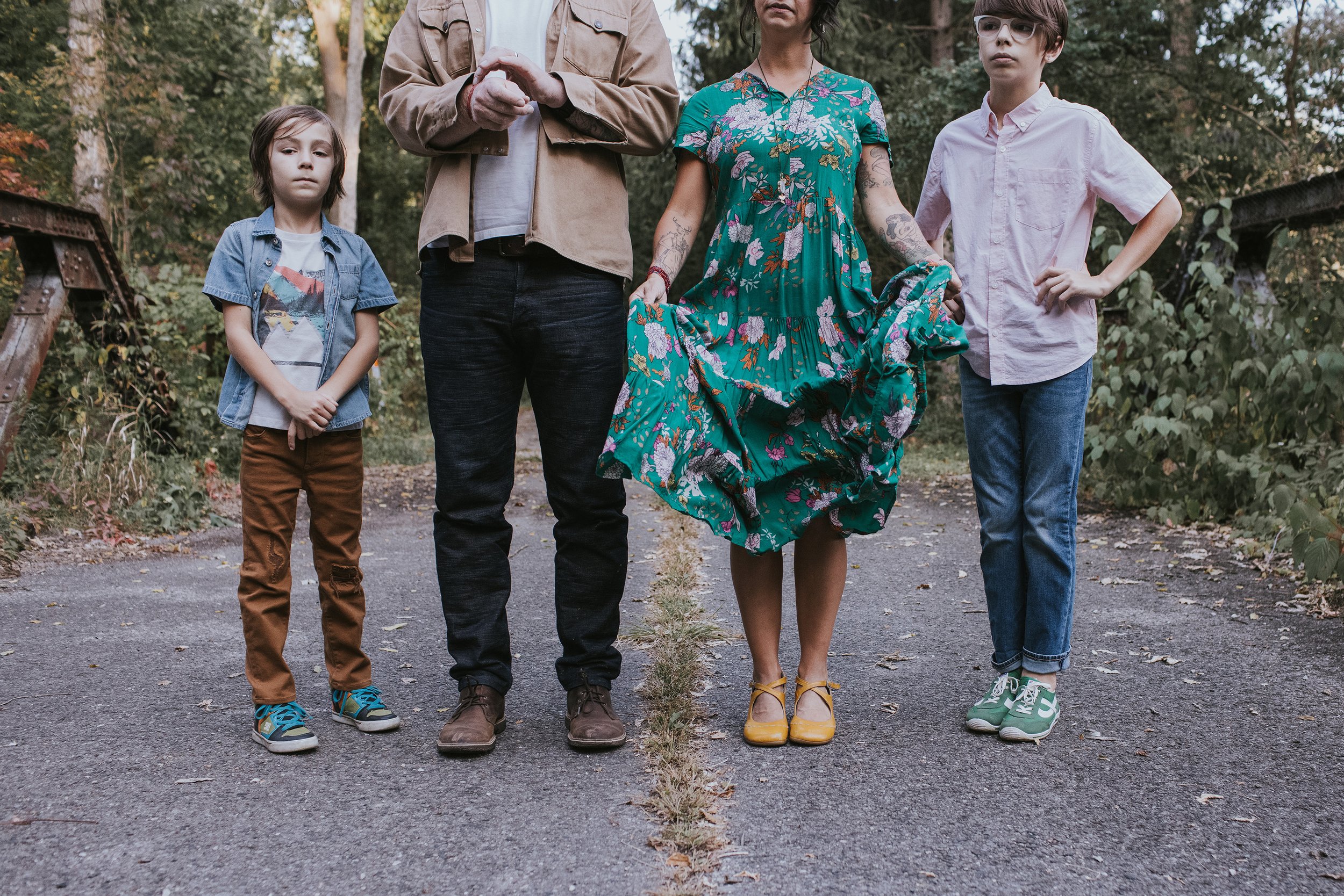 A family of four standing together on a forest path, each with their own unique style, captured in a creative and slightly whimsical portrait.