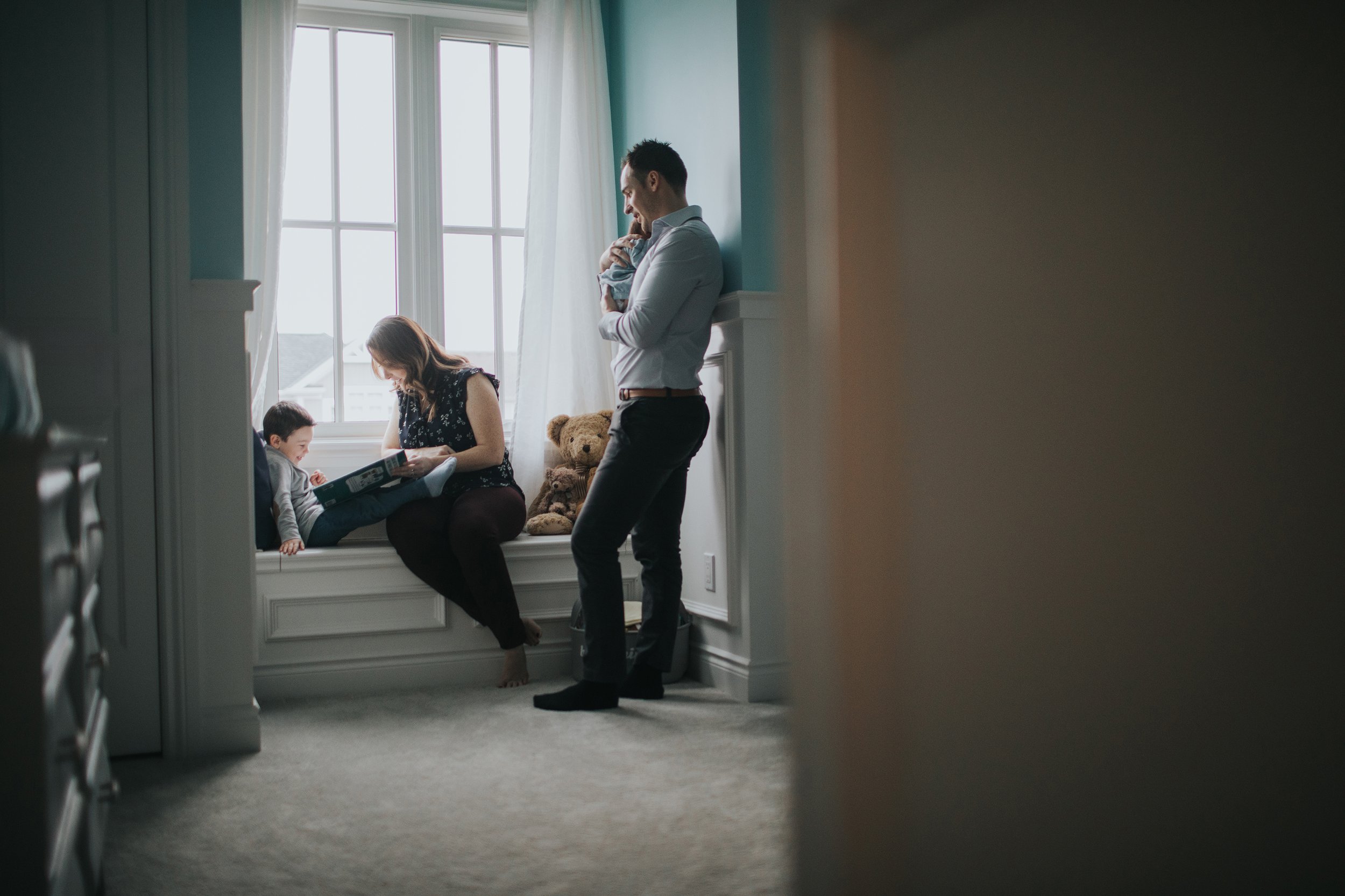 A cozy family scene with parents and a child reading a book together by the window in a softly lit bedroom.