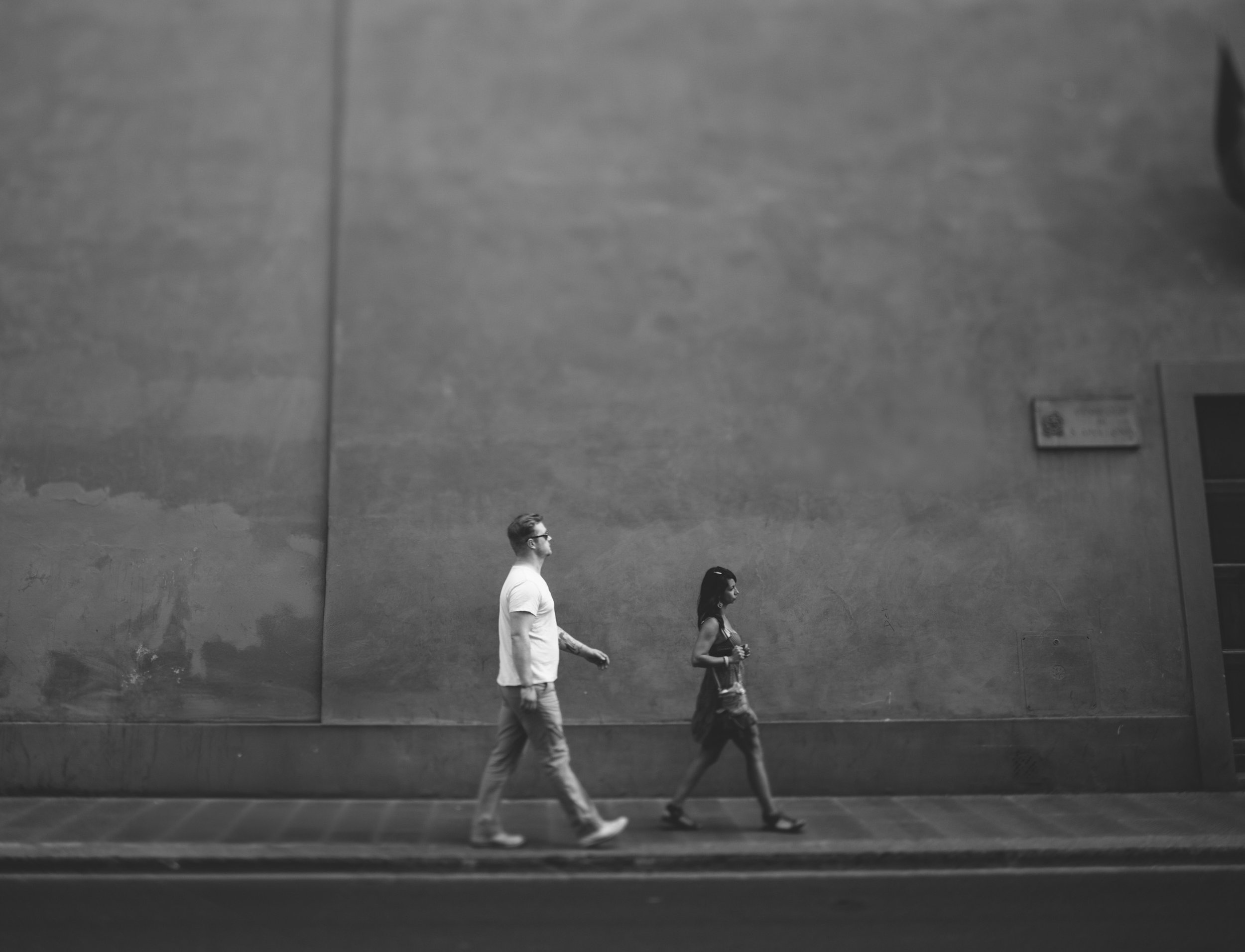 A couple walks side by side down an urban street in Italy, captured in a striking black-and-white photograph that emphasizes the simplicity and beauty of the moment.
