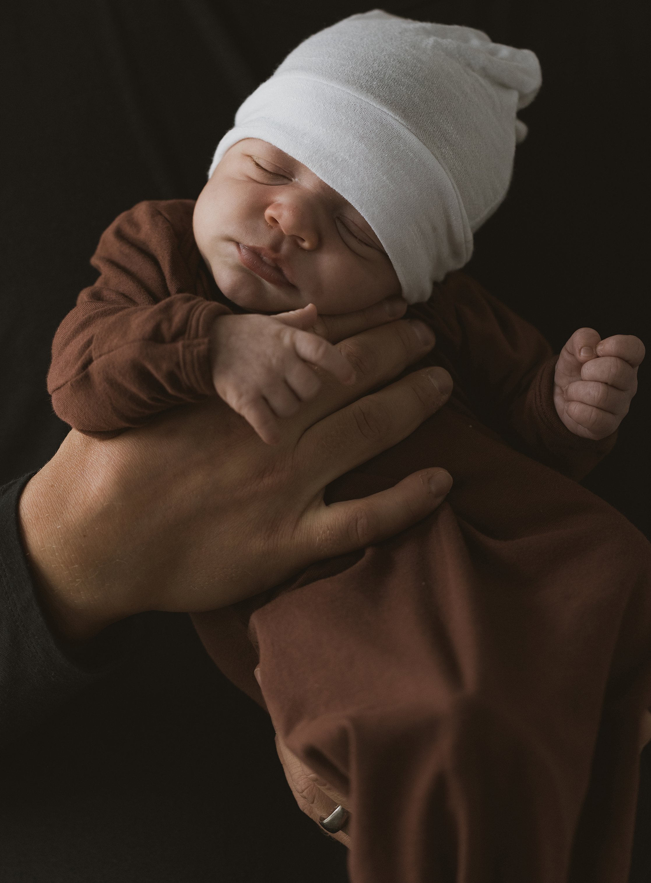A tender moment with parents lovingly holding their newborn baby, captured through a soft-focus lens, sitting by a large window.