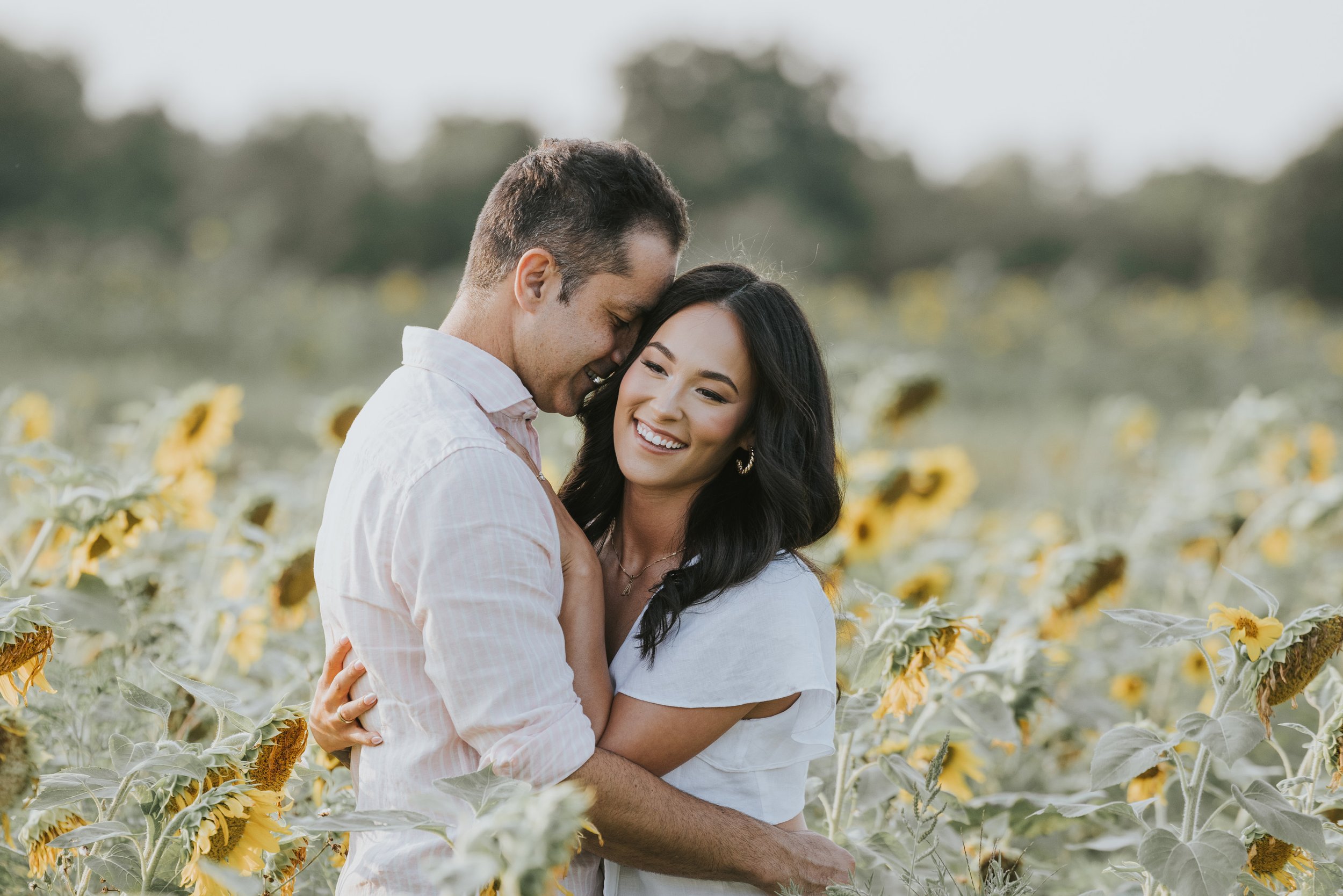A couple embracing and smiling in a sunflower field, capturing a joyful moment during their engagement session.