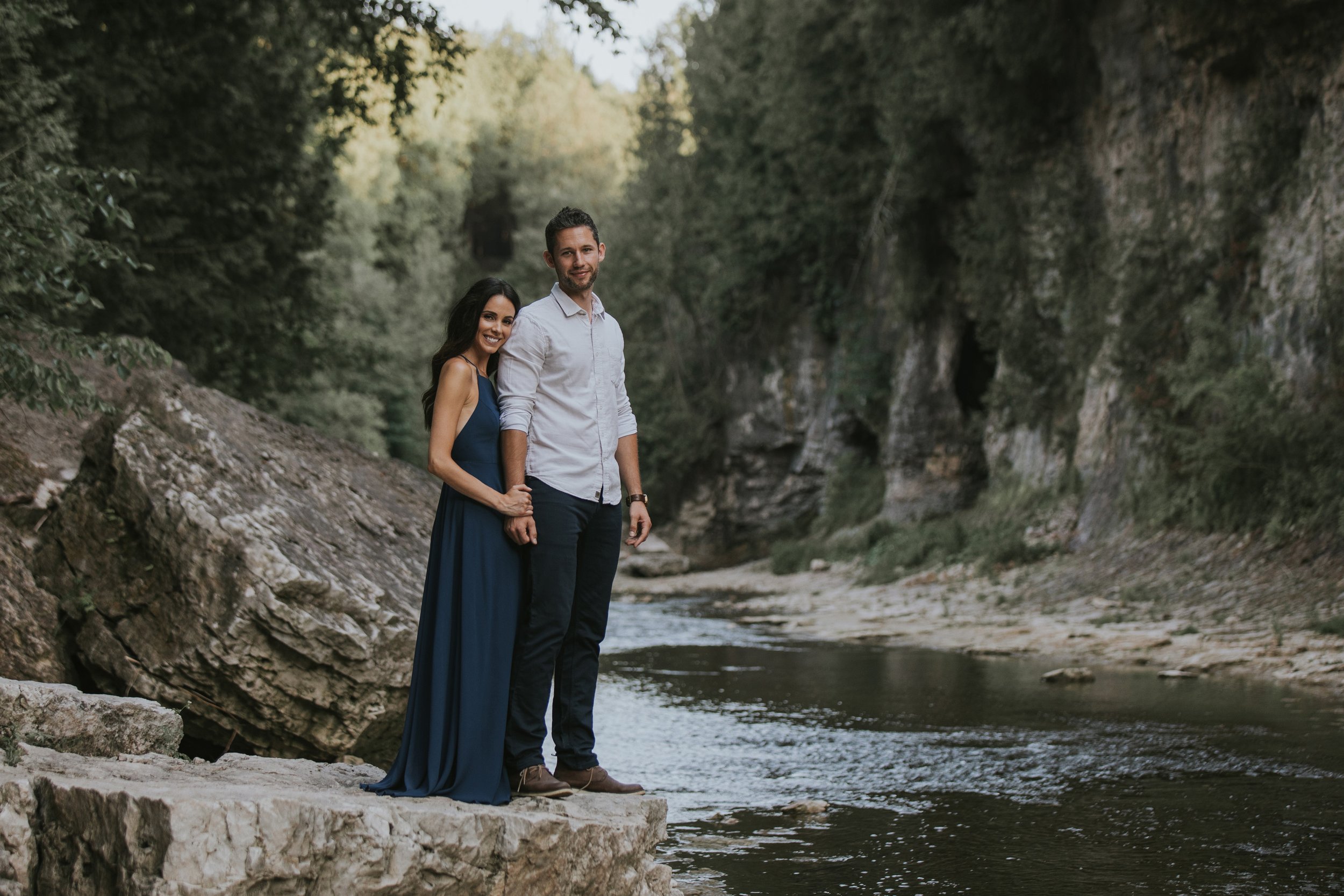 A couple standing hand-in-hand on rocks by the river in Elora Gorge, embraced by the natural beauty of the gorge.