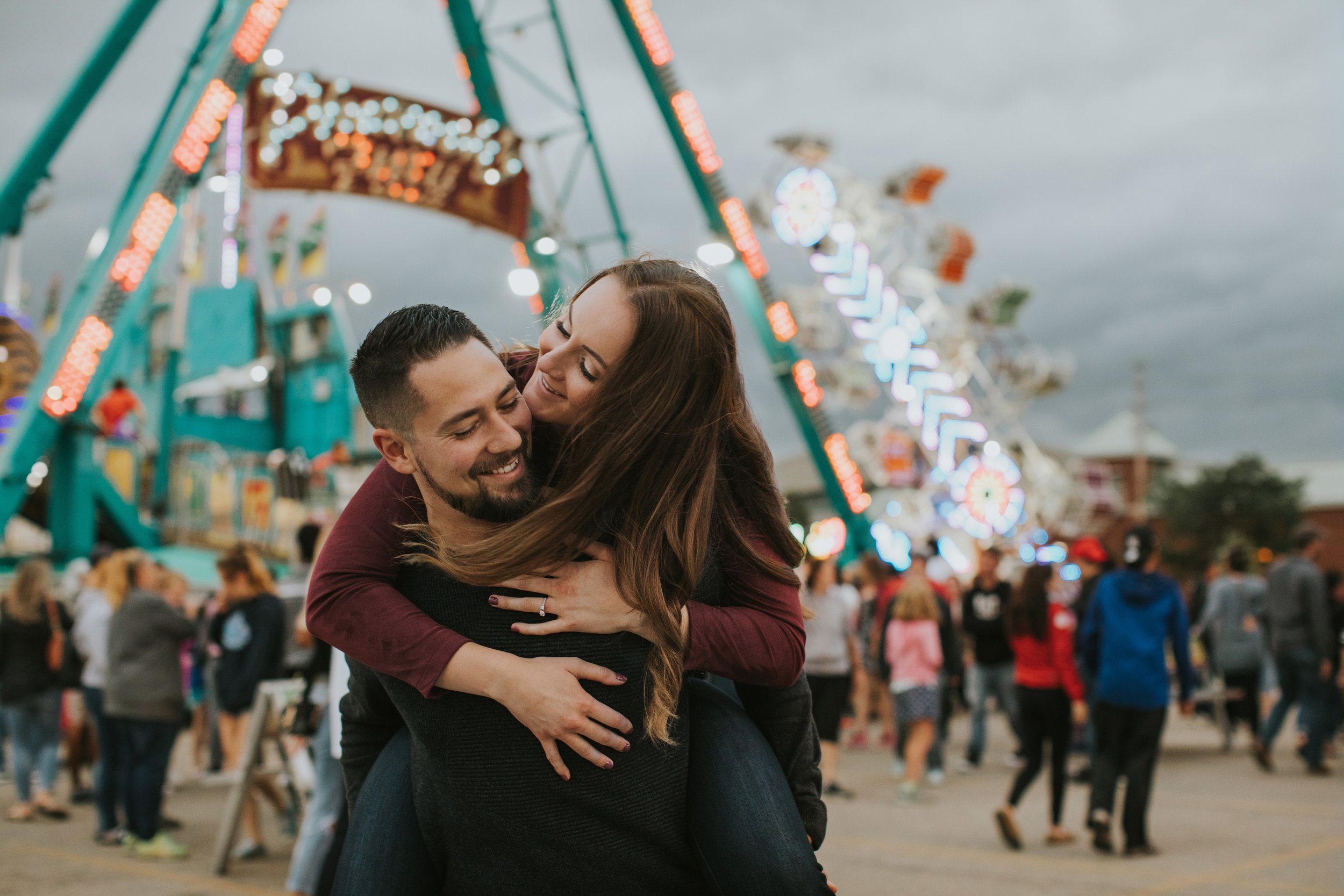 A playful moment of a couple enjoying a piggyback ride at a vibrant carnival, surrounded by bright lights and fun-filled attractions.