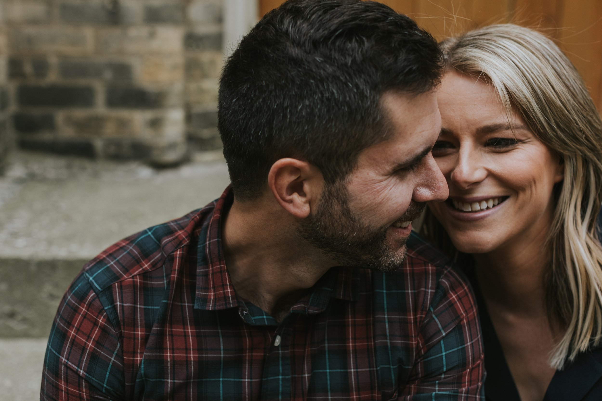 A couple smiling warmly at each other during an outdoor engagement shoot, showing their close bond.