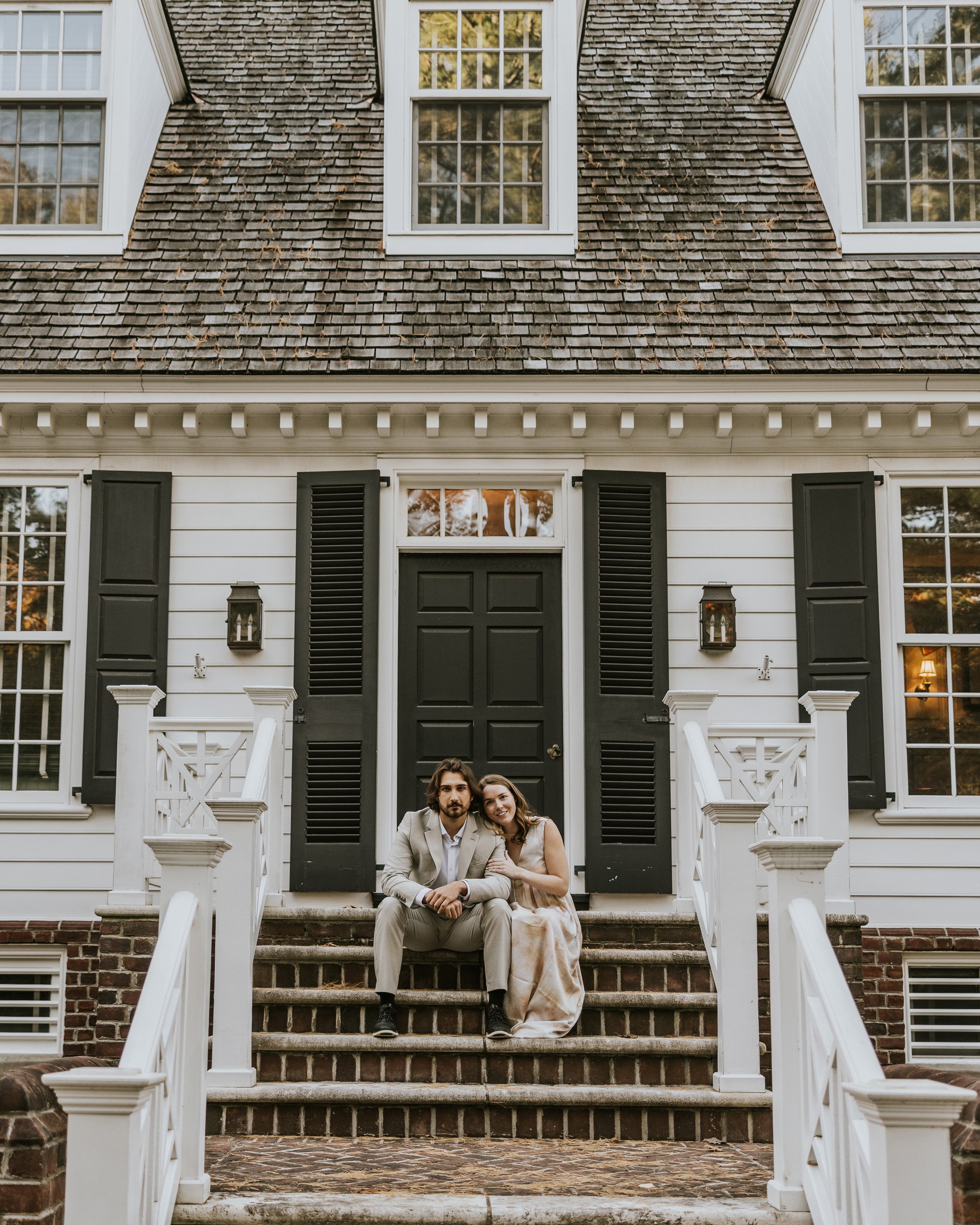 Couple sitting on the front steps of a traditional house, embracing and smiling, with a warm, rustic exterior in GrandBend, Ontario.