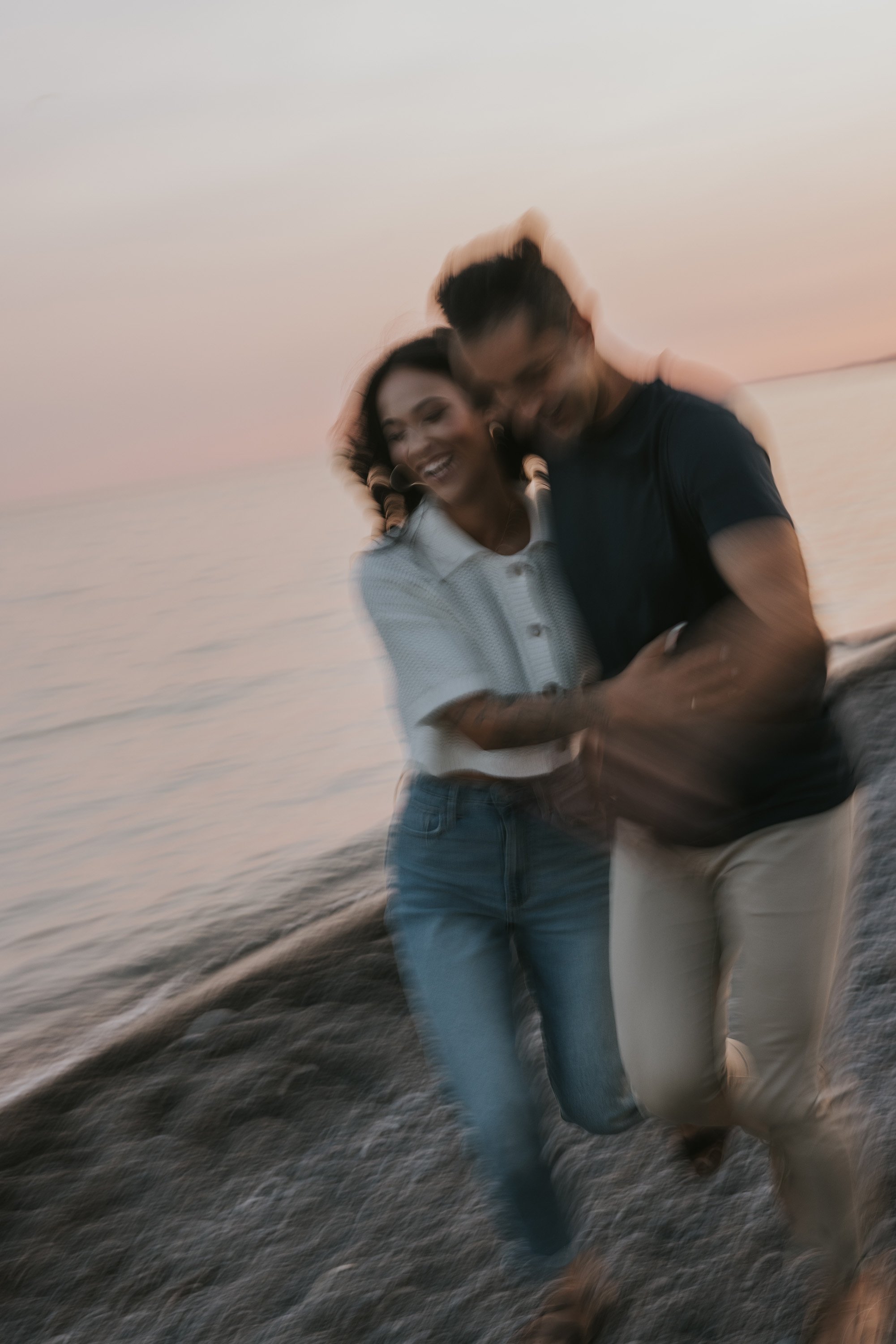 A fun and playful moment captured in motion blur as a couple runs along the beach at sunset.