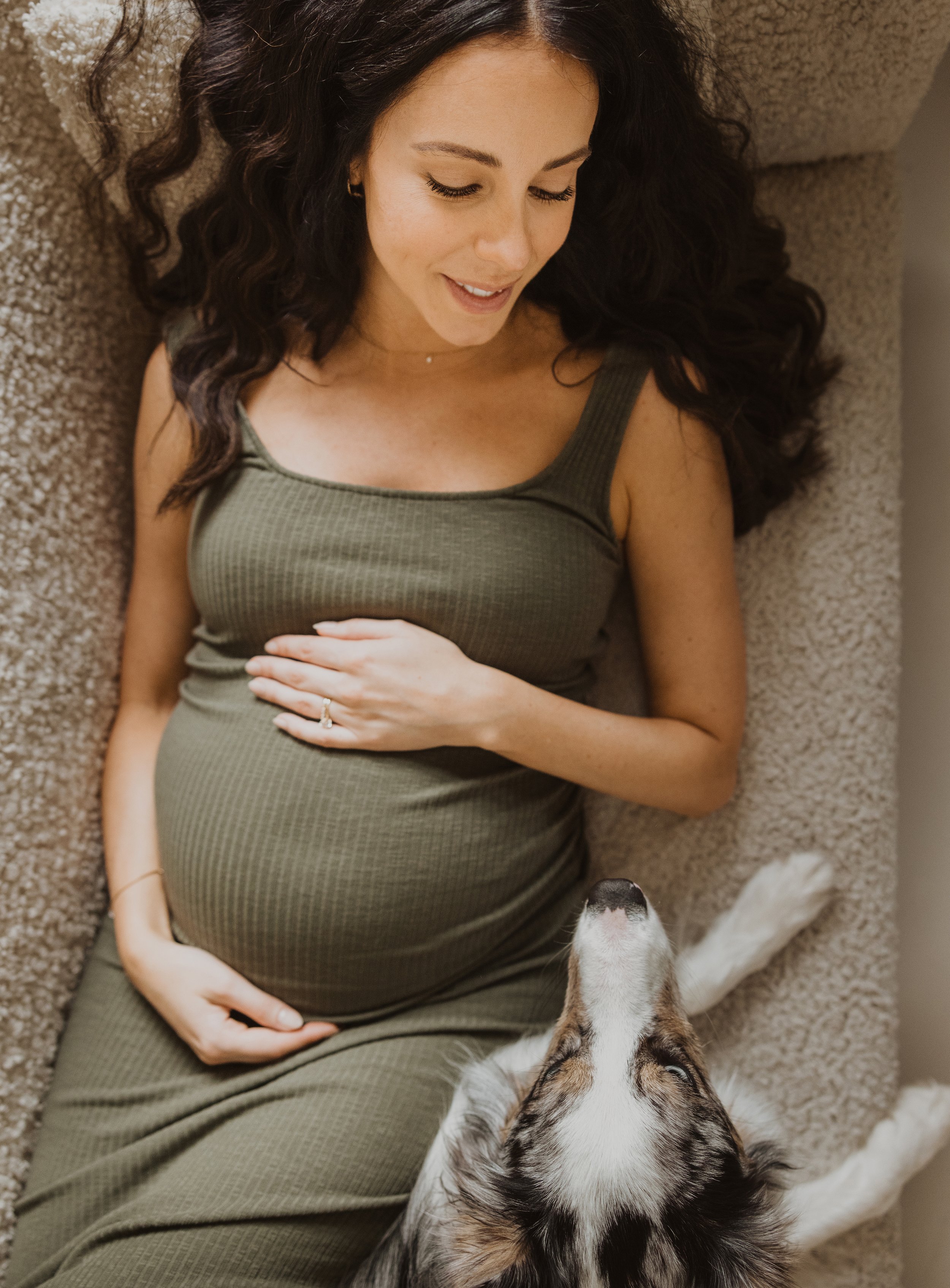 A cozy indoor portrait of a pregnant woman lying on a sofa, with her loyal dog resting beside her.